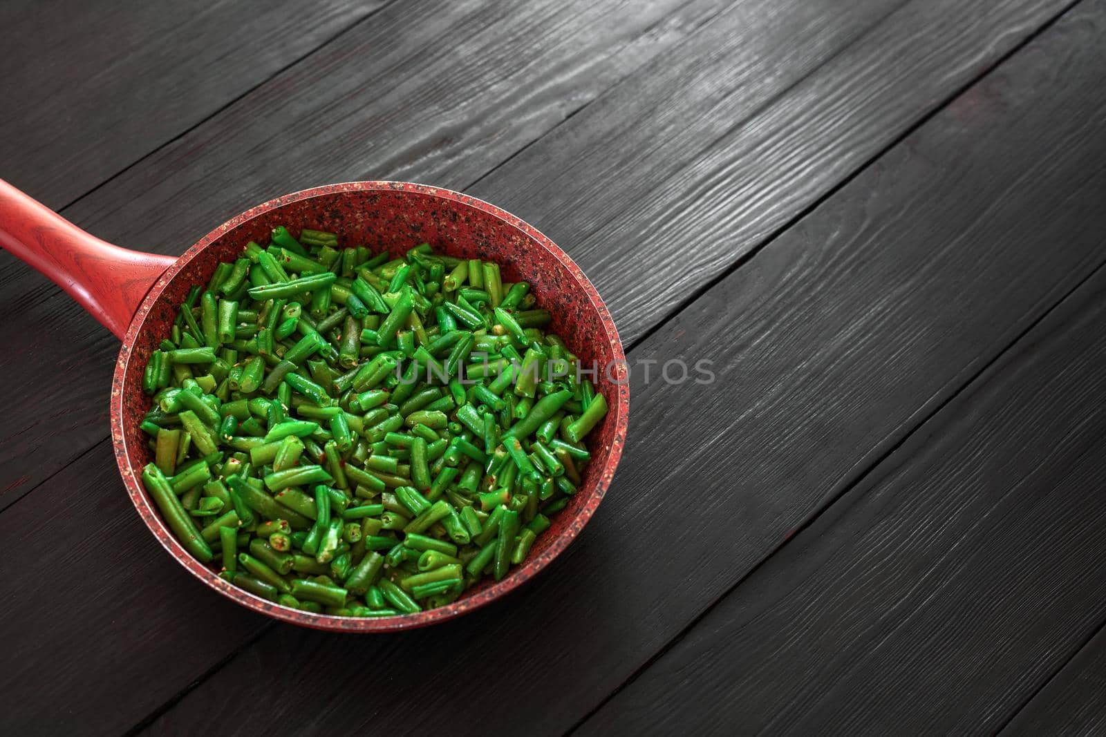 Cooked green beans in a frying pan on a black wooden background. Space to copy. Top view .