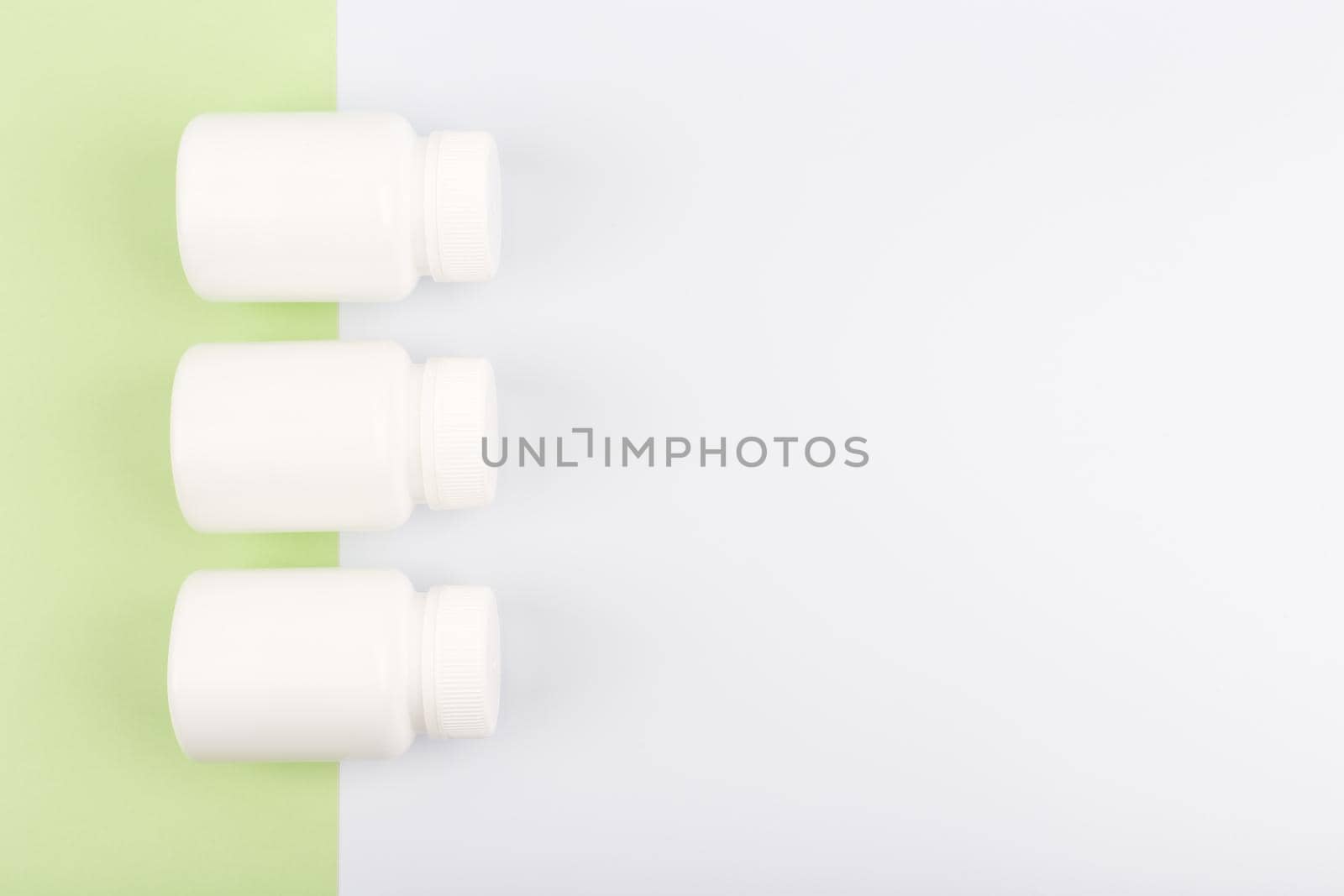 Top view of three white glossy medication bottles in a row on light green and white background with space for text. High quality photo