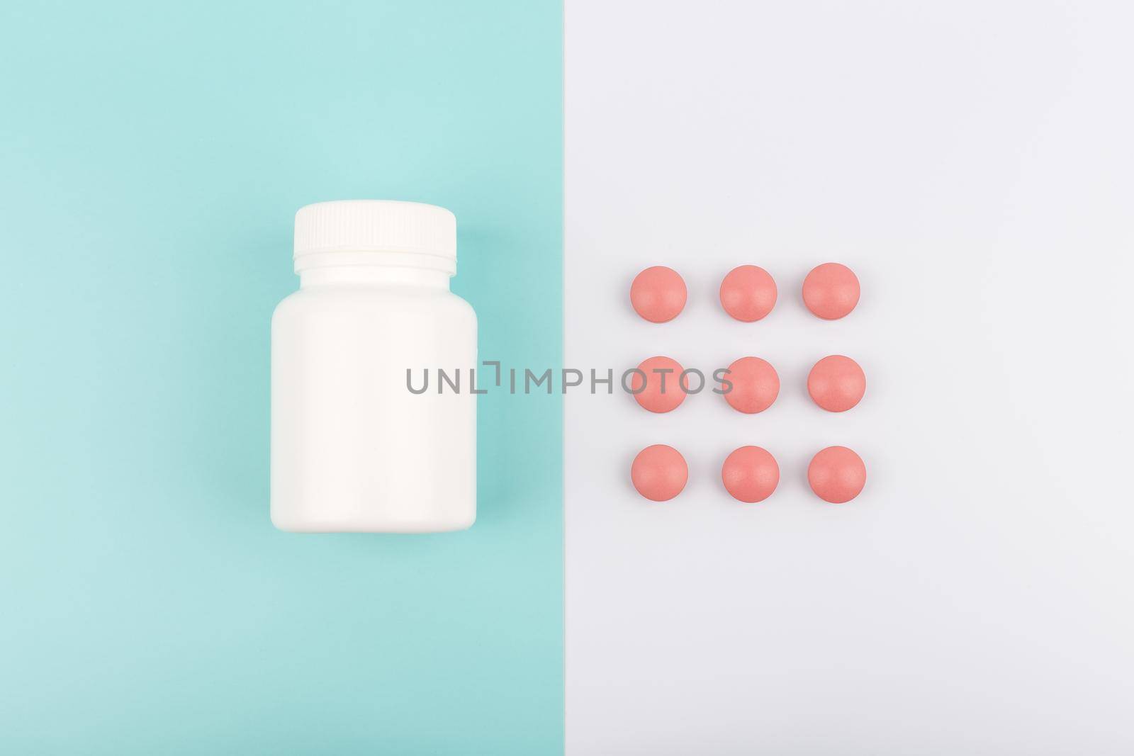 Flat lay with white glossy medication bottle and red round pills on blue and white background in light tones by Senorina_Irina