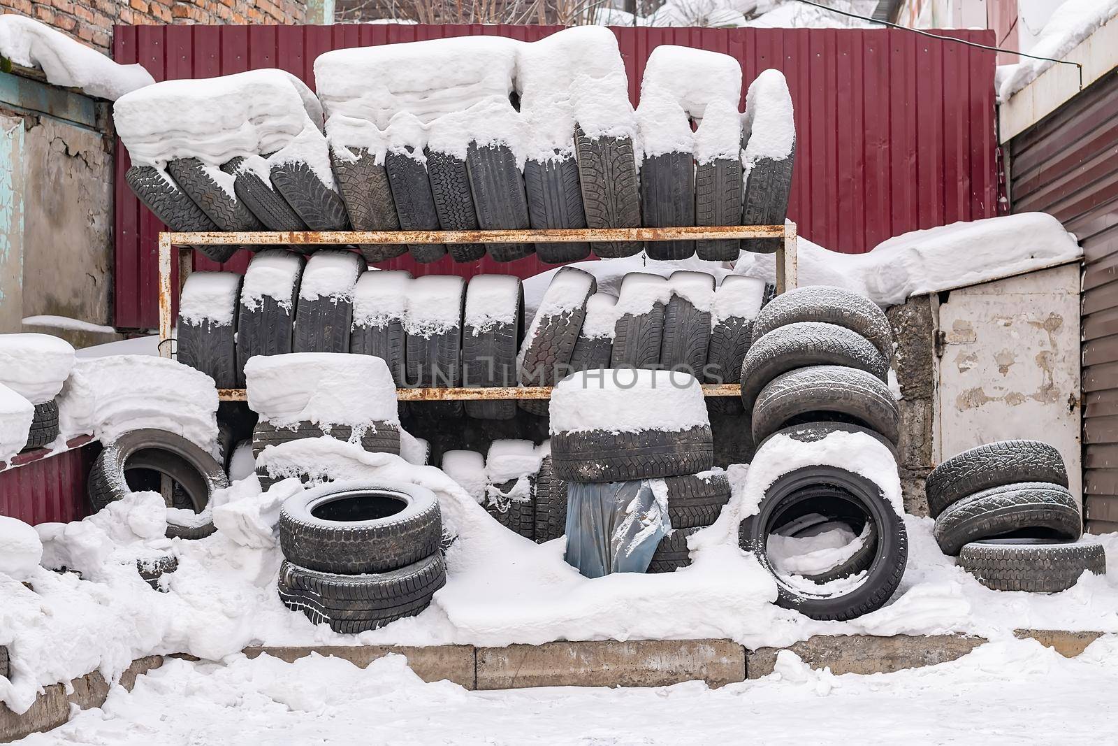 a lot of, a pile of worn-out, used car tires, tire wheels lie on a rack outdoor in the winter in the snow