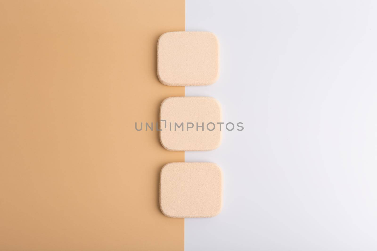 Top view of three square shaped make up sponges on beige and pink background. High quality photo
