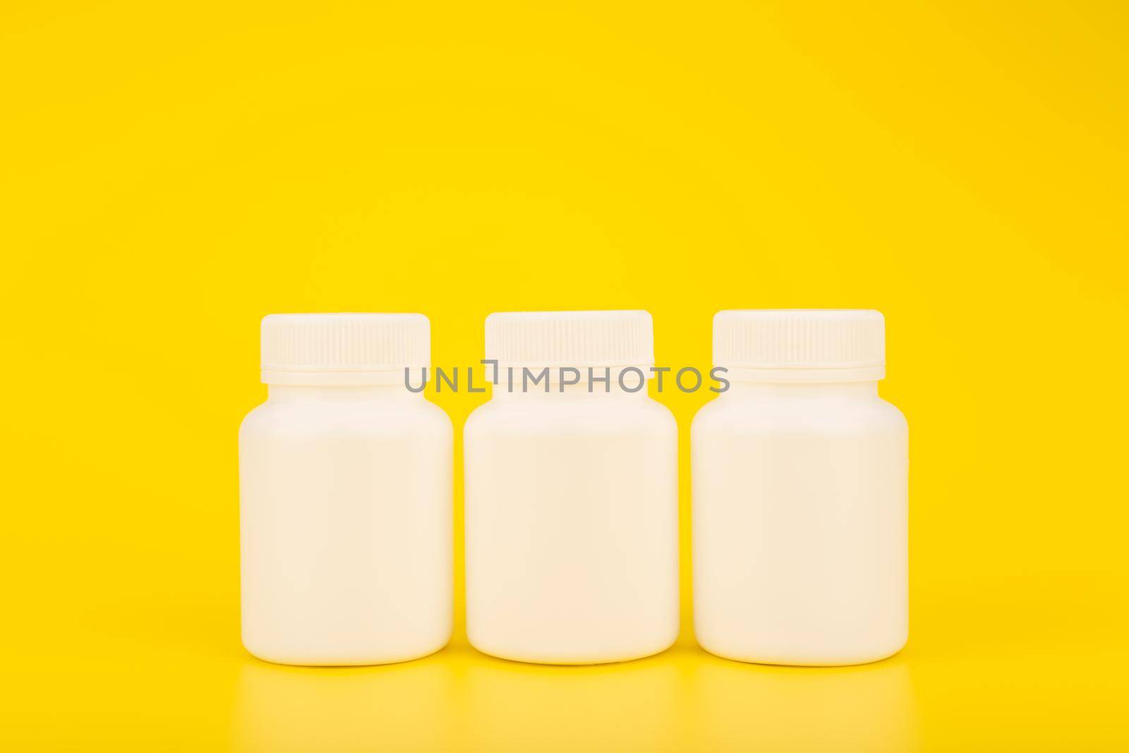 Creative minimalistic still life with three white plastic medication bottles in a row on yellow background. Concept of health and wellness