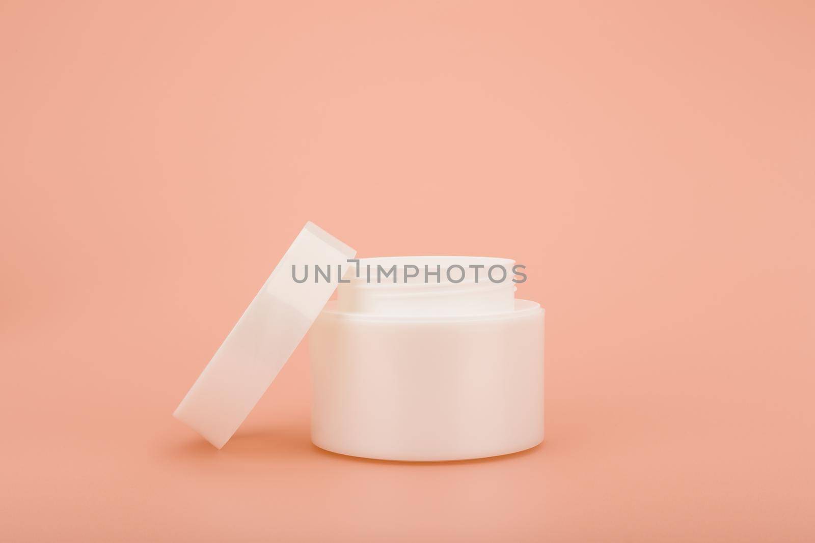 Minimalistic still life with white glossy opened cream jar on beige background with space for text