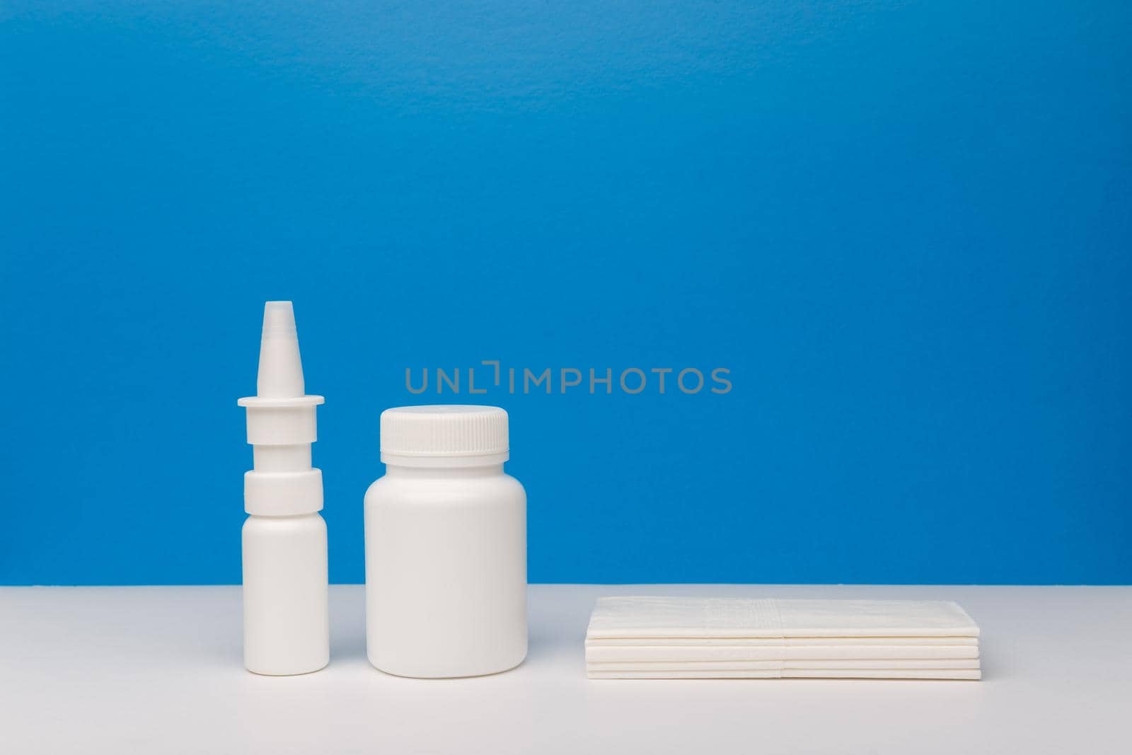 Minimalistic still life with nose spray, white plastic medication bottle and napkins against blue background. High quality photo