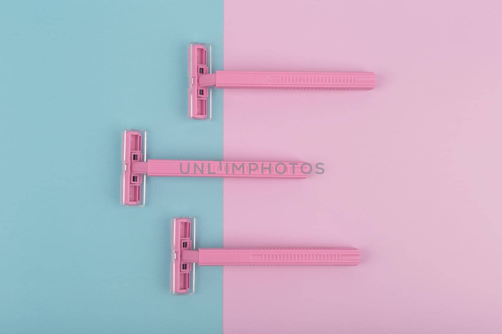 Top view of three pink plastic razors on colored background. Hair removal concept