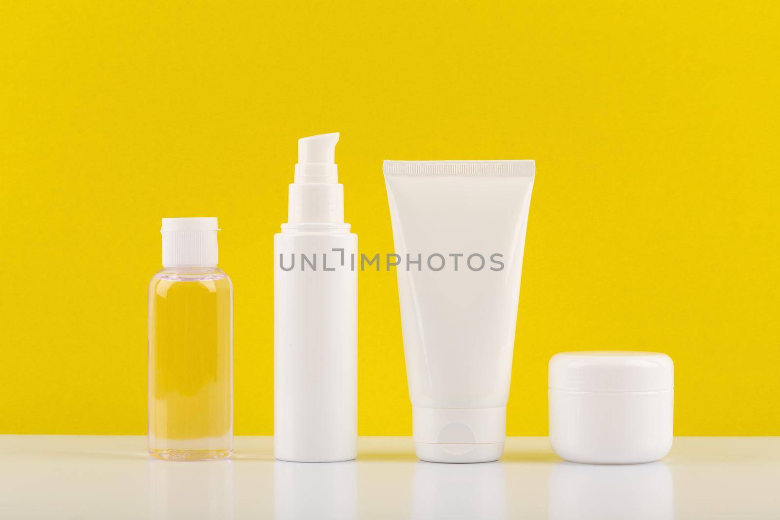 Still life with a set of cosmetic products on white table against bright yellow background. Concept of daily skincare or summer skin care