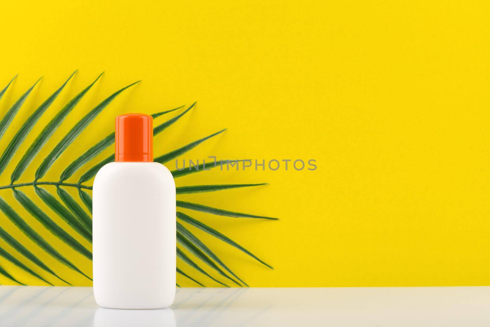 Sunscreen lotion in white jar with orange cap against yellow background with a palm with space for text by Senorina_Irina