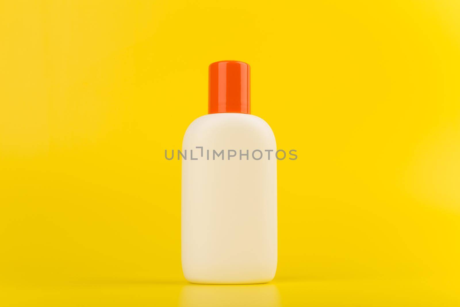 Minimalistic still life with sunscreen cream or lotion with orange cap on yellow background with space for text. Concept of summer skin care and protection