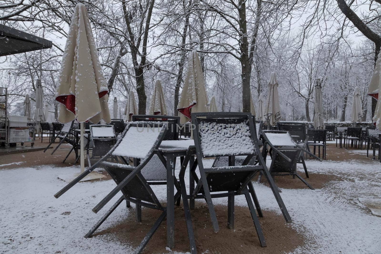 Madrid, Spain - January 07, 2021: Tables and chairs on a terrace, collected, without customers, in the Buen Retiro park in Madrid, in the middle of a snowy day, due to a wave of polar cold.