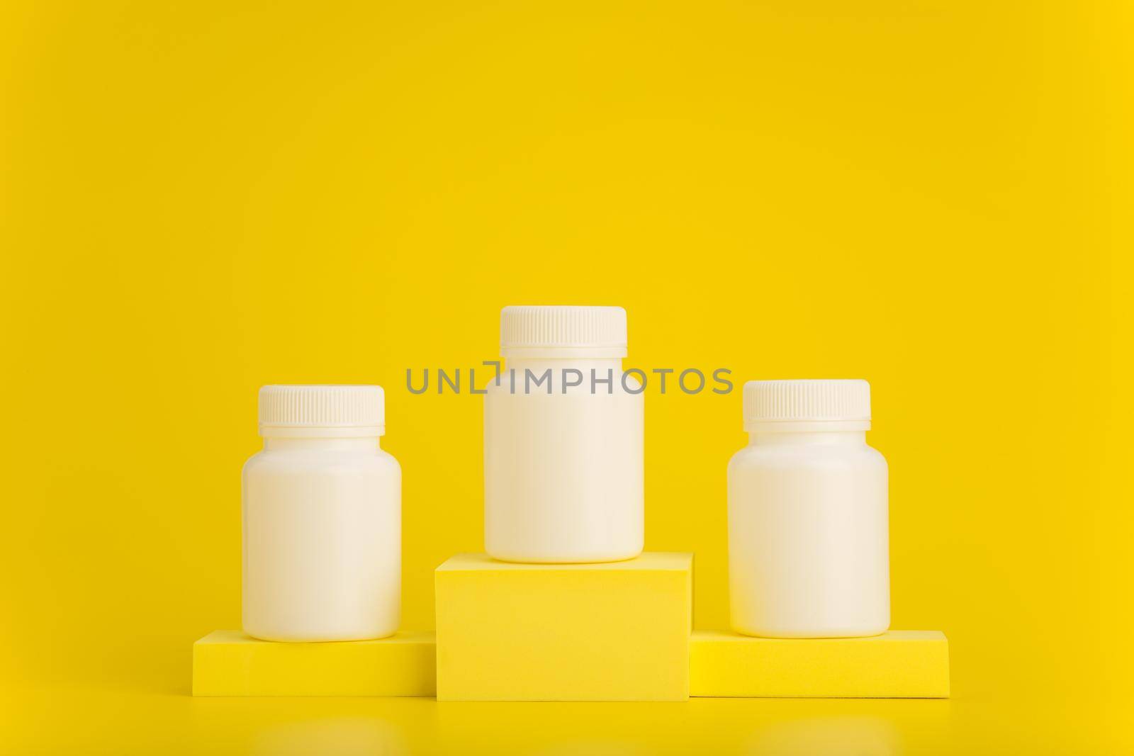 Three white unbranded medication bottles on yellow winner pedestal against yellow background with space for text. 