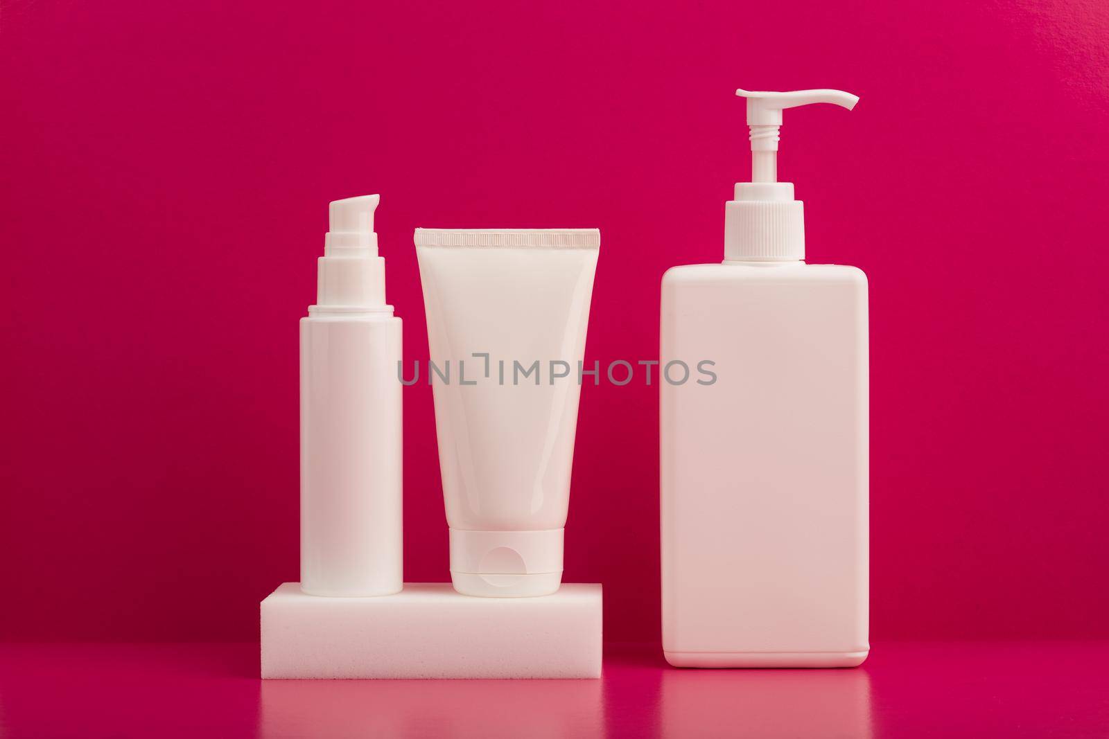 Still life with a set of creams or lotions on white podium against pink background on pink table. Concept of beauty treatment and every day skin routine