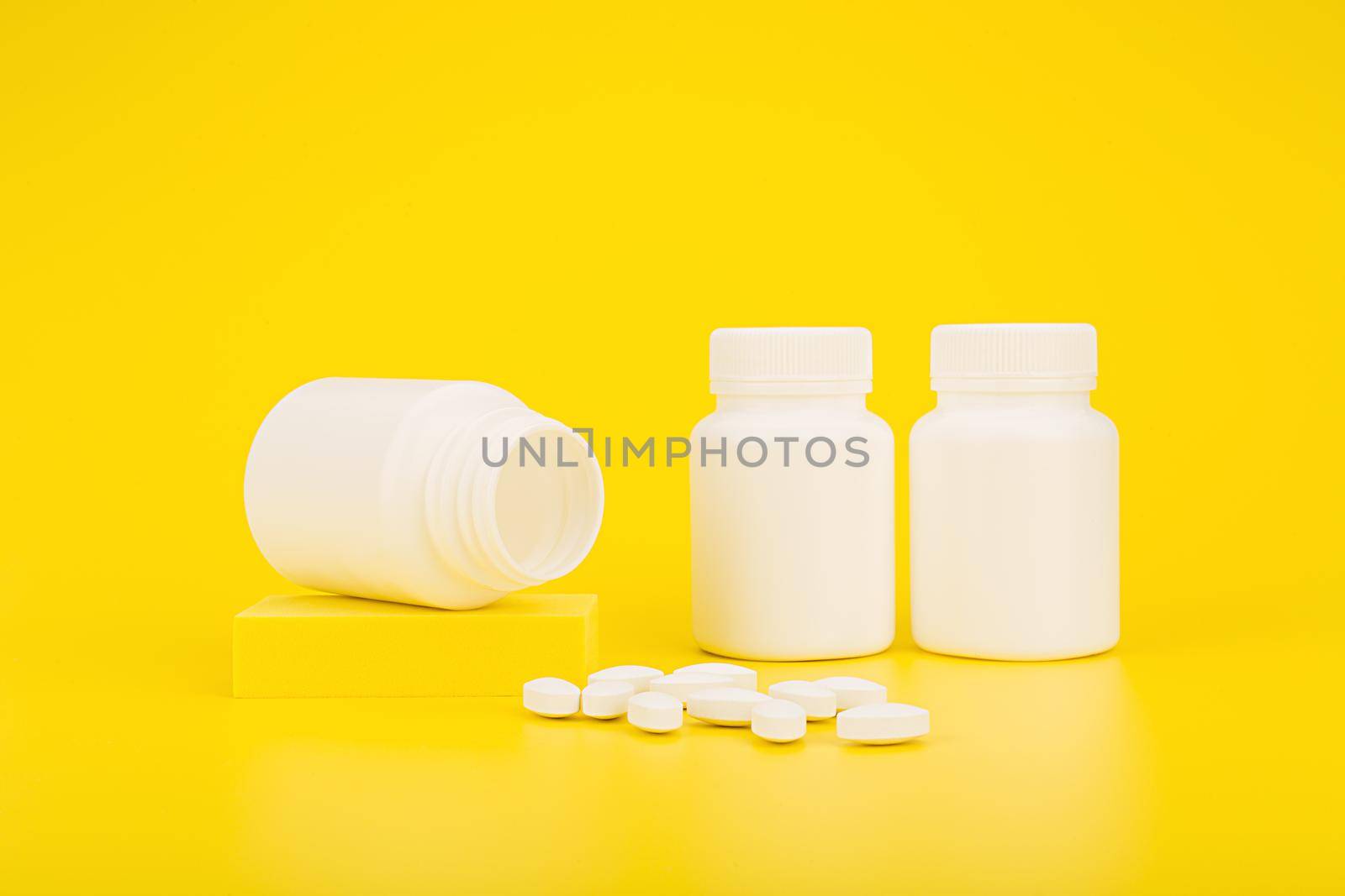 Bright till life with medication bottles and spilled pills on yellow background. The concept of pharmacy, health care and wellbeing or vitamins for kids