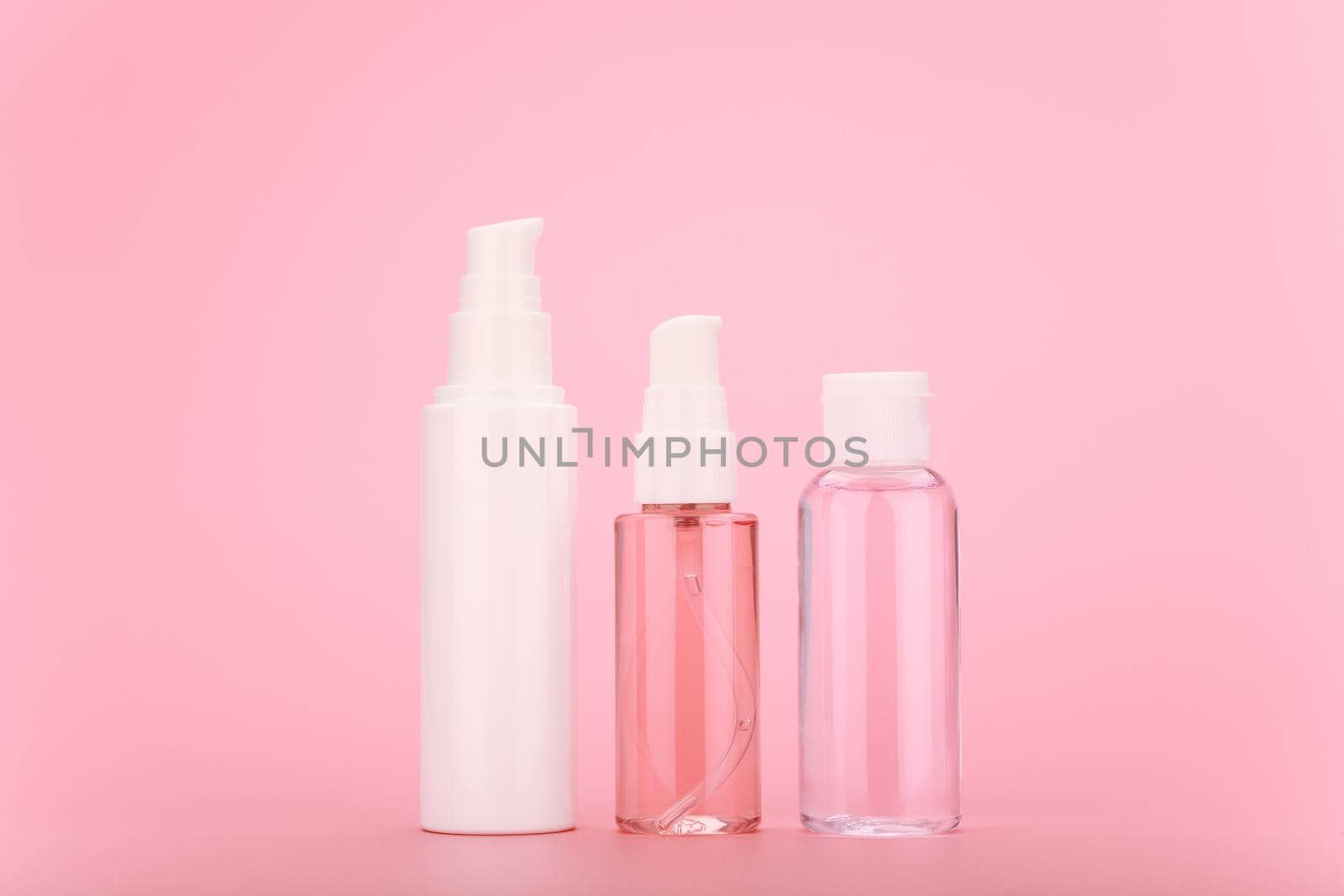 Face cream, cleaning foam or gel and lotion in transparent bottle with white caps against bright pink background by Senorina_Irina