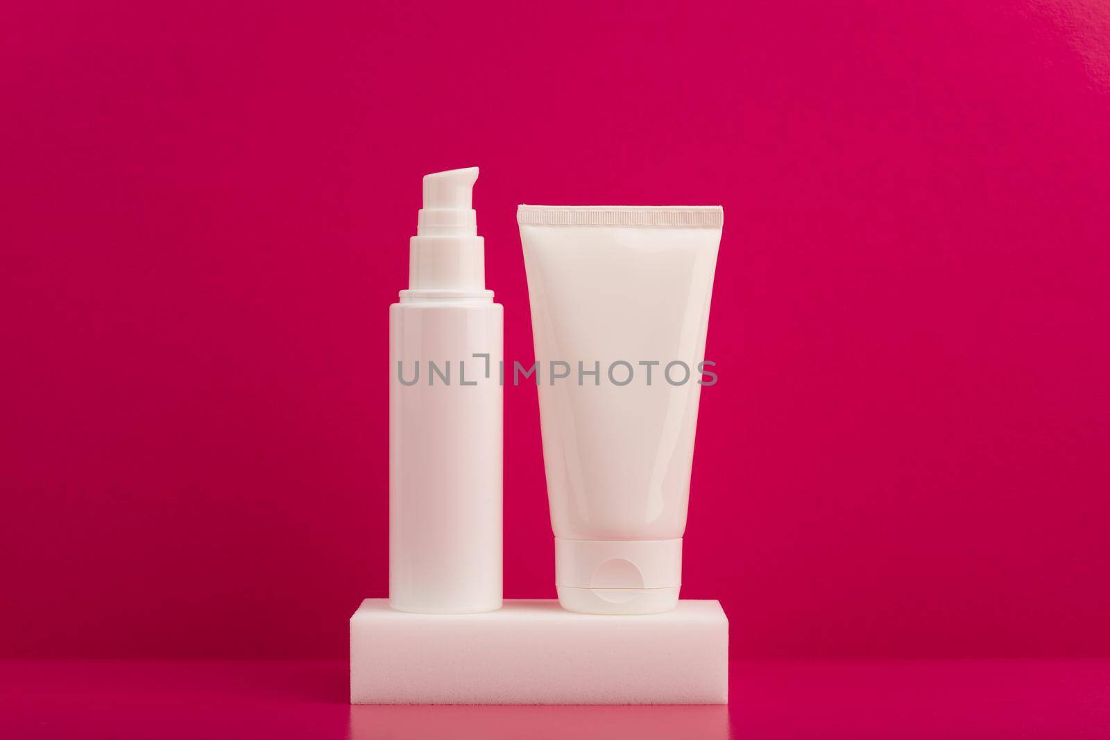 Two white unbranded cream tubes on white podium against pink background. Concept of skincare and beauty products by Senorina_Irina