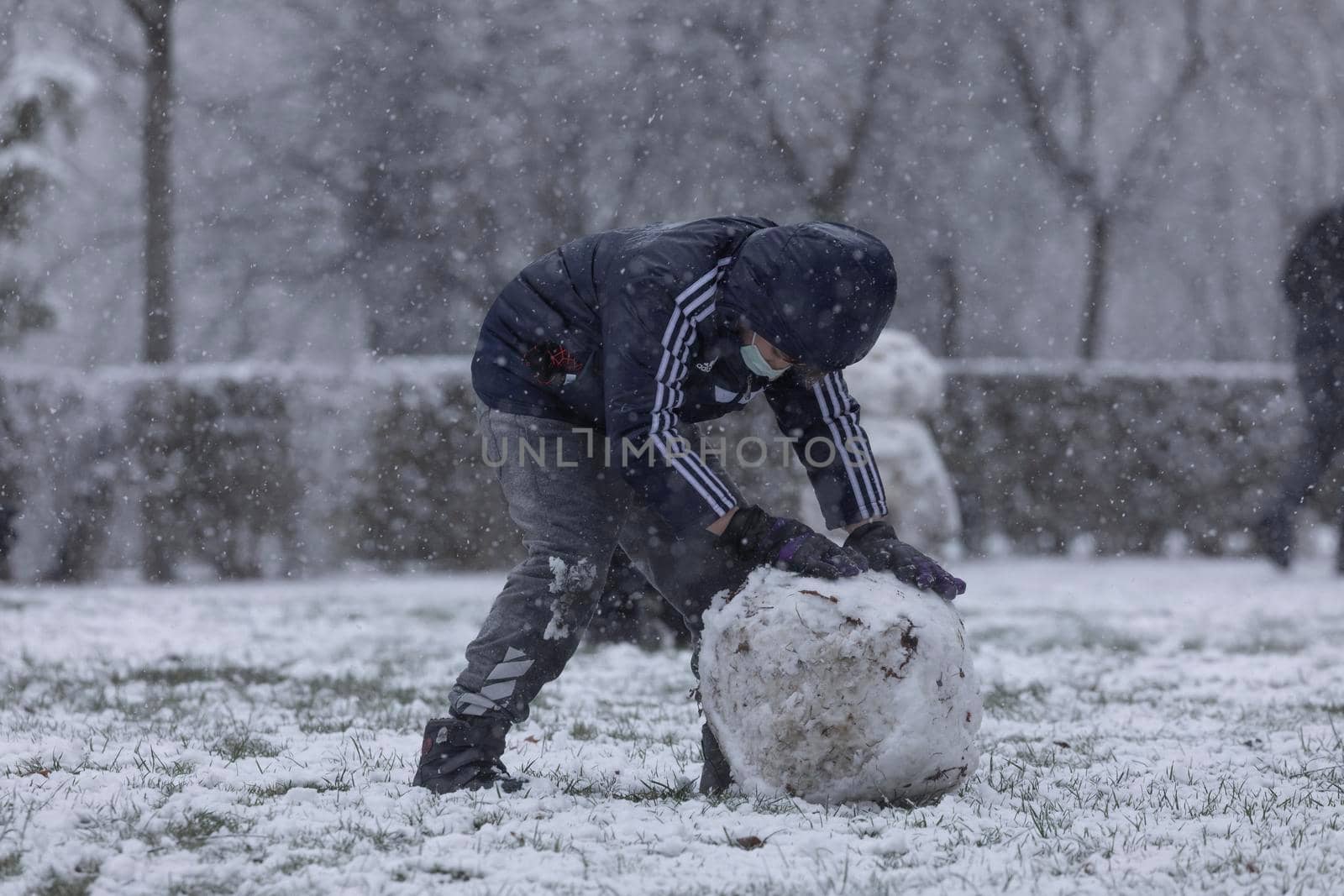 Madrid, Spain - January 07, 2021: Children playing with snow and making snowmen, in the Buen Retiro park in Madrid, in the middle of a snowy day, due to a wave of polar cold.