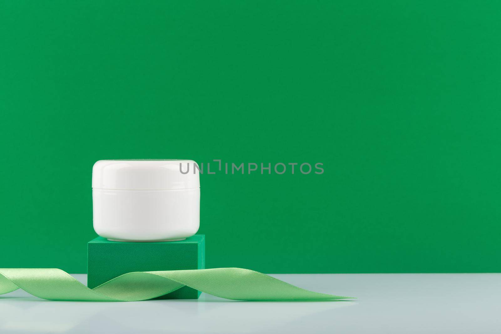 White cream, mask or balm jar on green podium with a ribbon against green background with copy space by Senorina_Irina