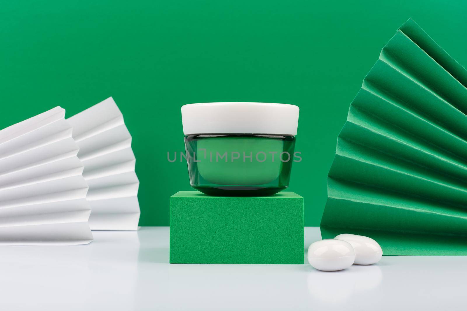 Green cream jar on green podium on white table against green decorated background. Concept of luxurious organic skincare by Senorina_Irina