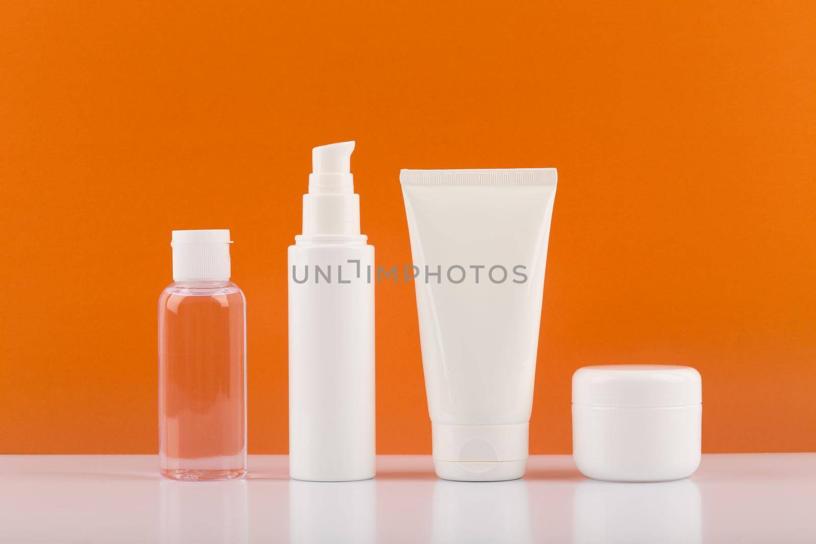 Set of skincare cosmetics on white glossy table against orange background. Concept of skincare and wellbeing by Senorina_Irina