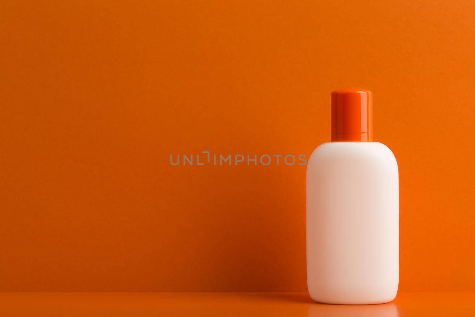 Minimalistic still life with sunscreen cream or lotion with orange cap on orange background with space for text. Concept of skin protection during summer and safe tan