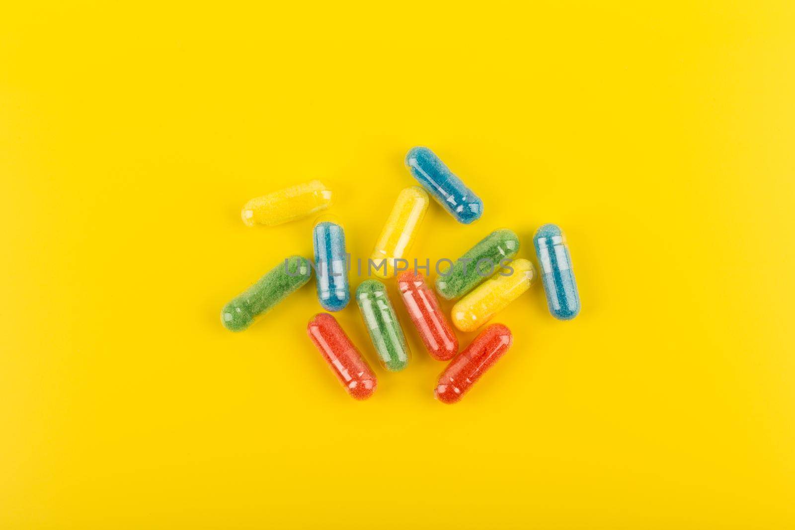 Minimalistic flat lay with spilled green, red, blue and yellow pills on bright yellow background. High quality photo