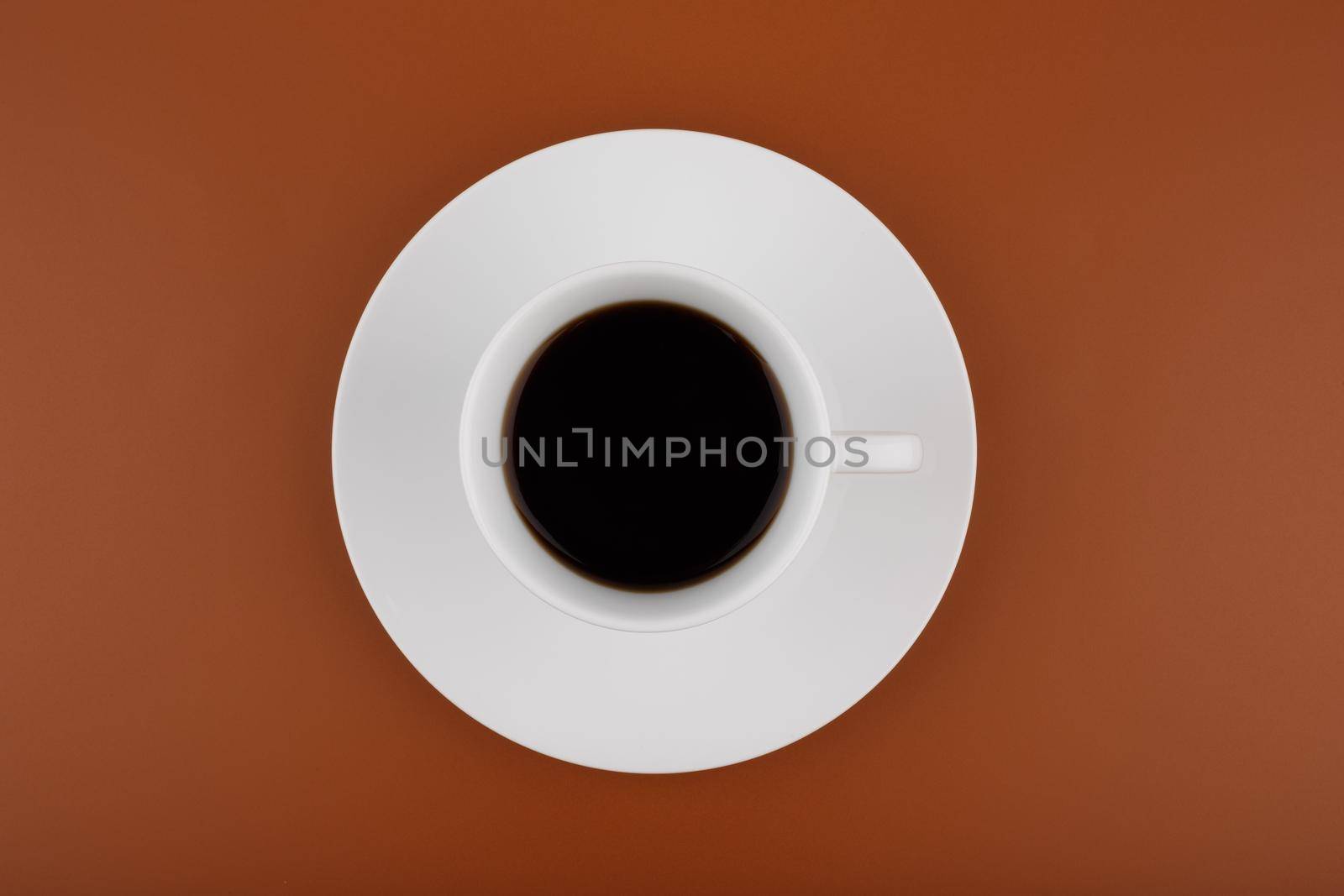 Top view of white ceramic coffee cup on a plate against brown background