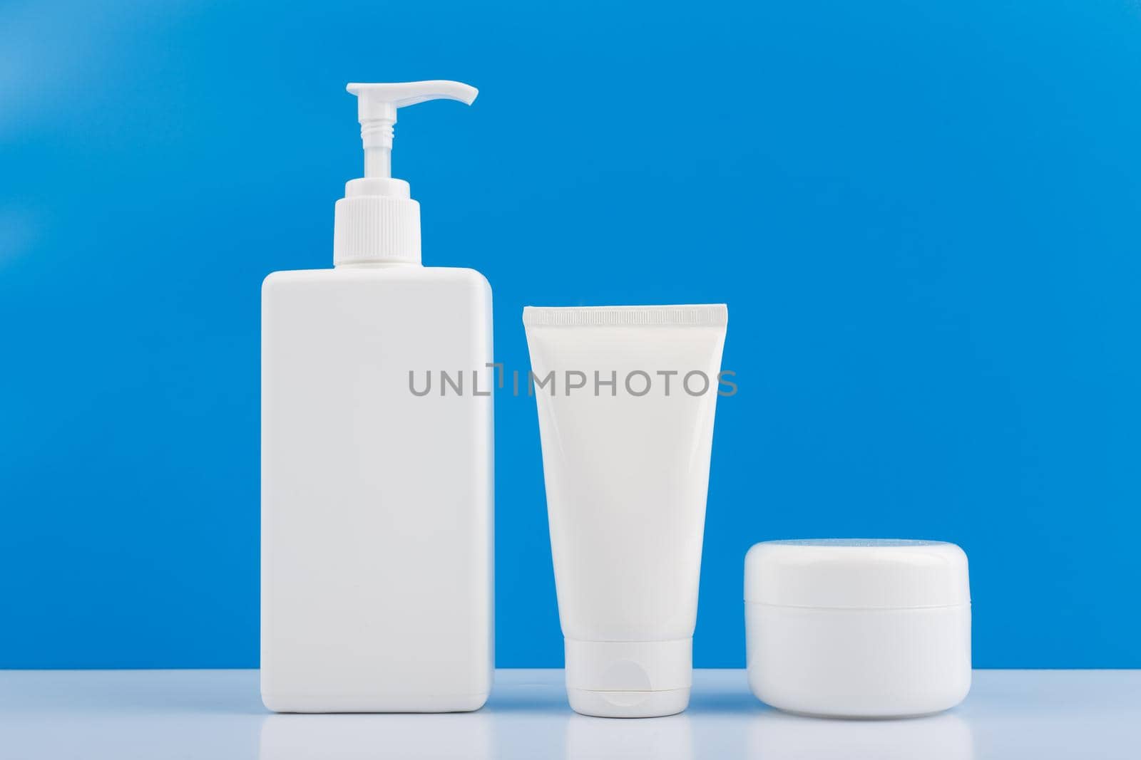 Set of cosmetic products for men skincare and hygiene on white glossy table against blue background. Concept of promotion and advertising of beauty treatment