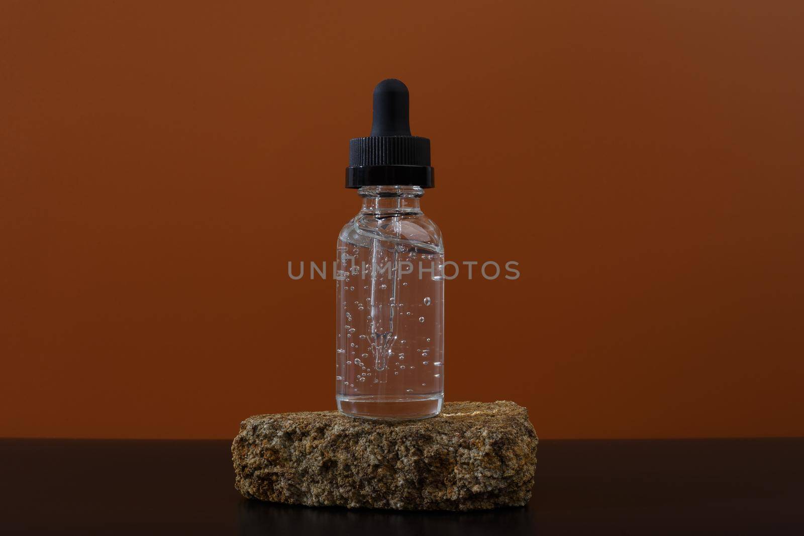 Still life with skin serum in transparent bottle on a stone and black table against brown background. High quality photo