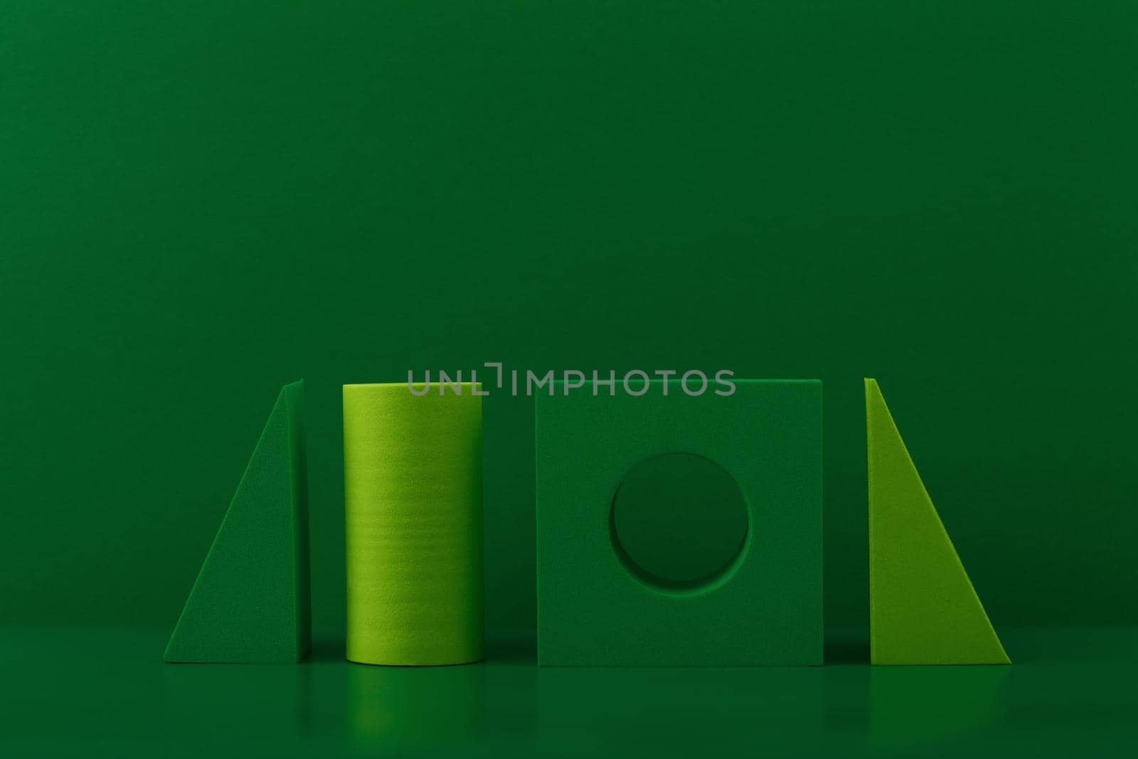 Simple monochromatic still life with light and dark green geometric figures on green background with space for text