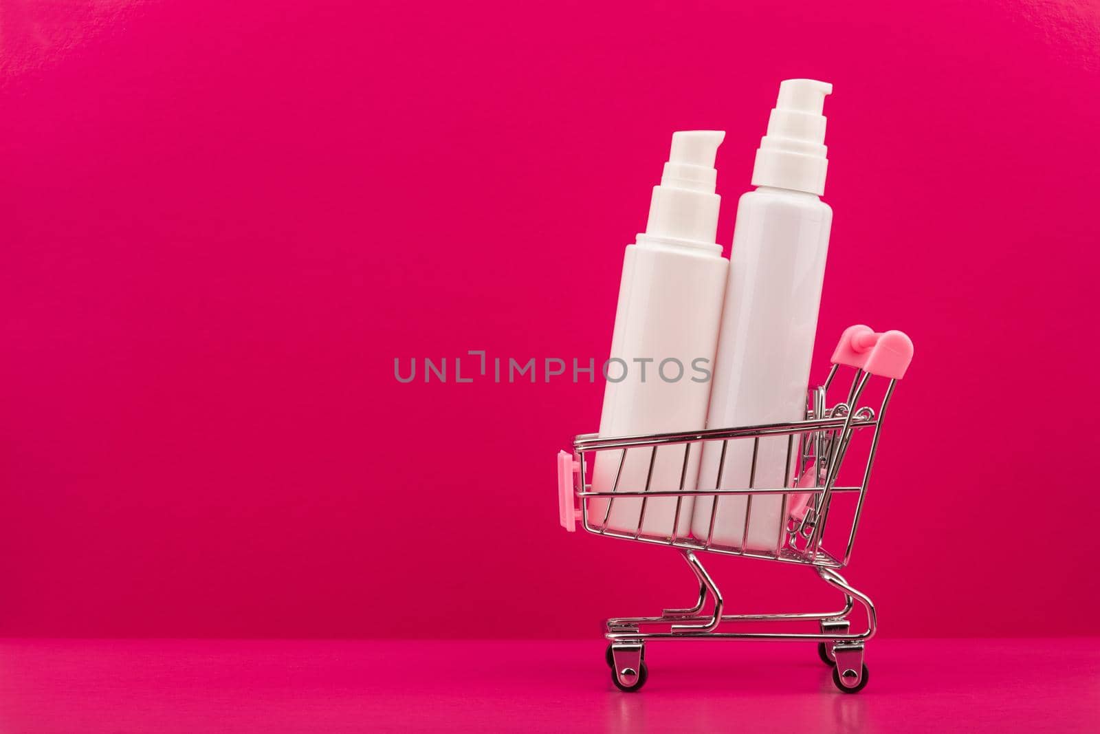 Shopping cart with face creams on pink background with space for text by Senorina_Irina