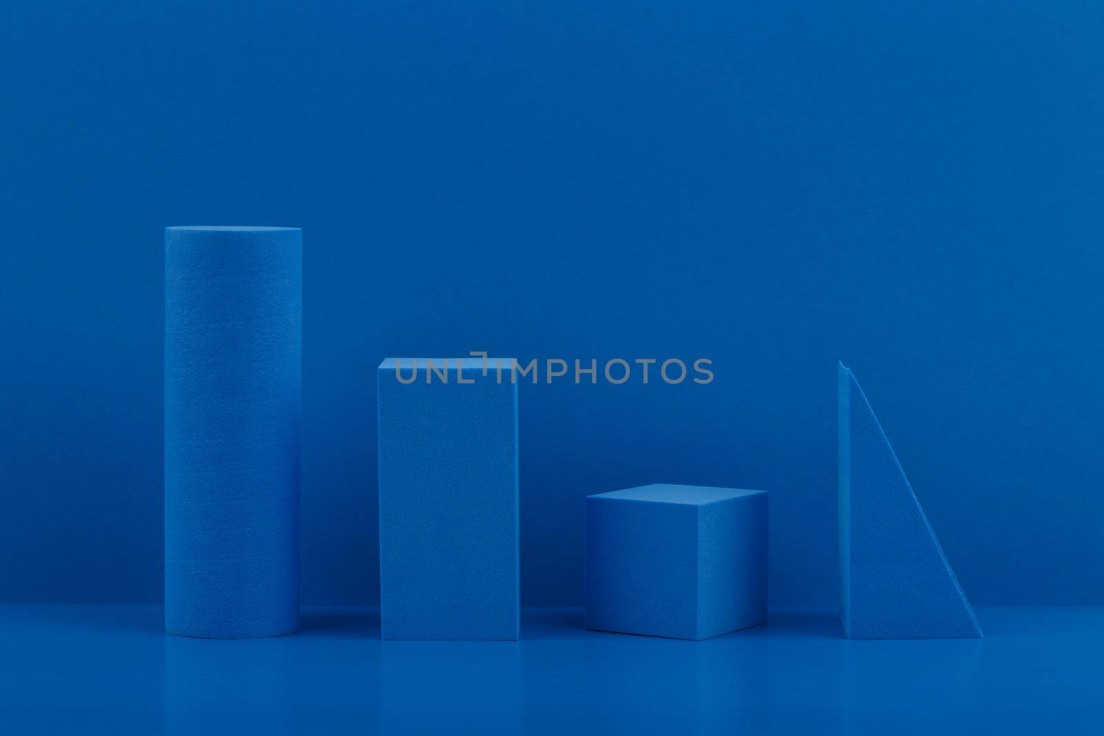 Blue cylinder, rectangular, square and triangle on blue table against blue background
