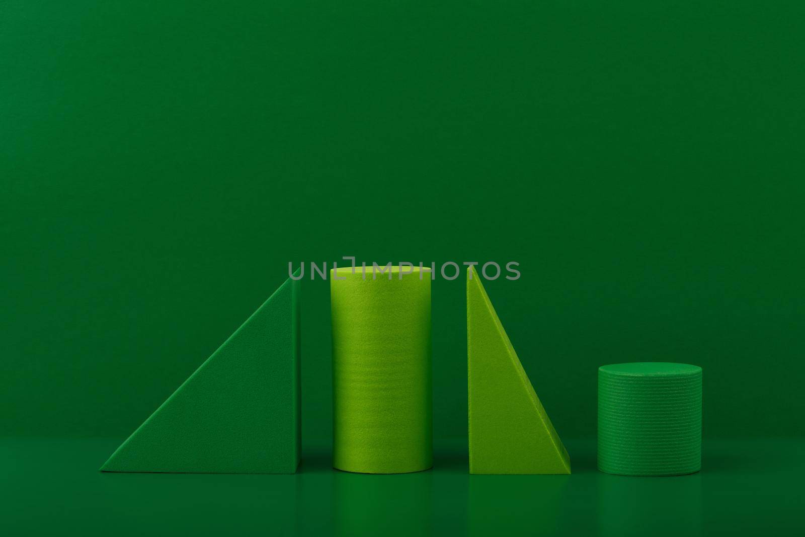 Abstract still life with light and dark green geometric figures triangles and cylinders against green background. 