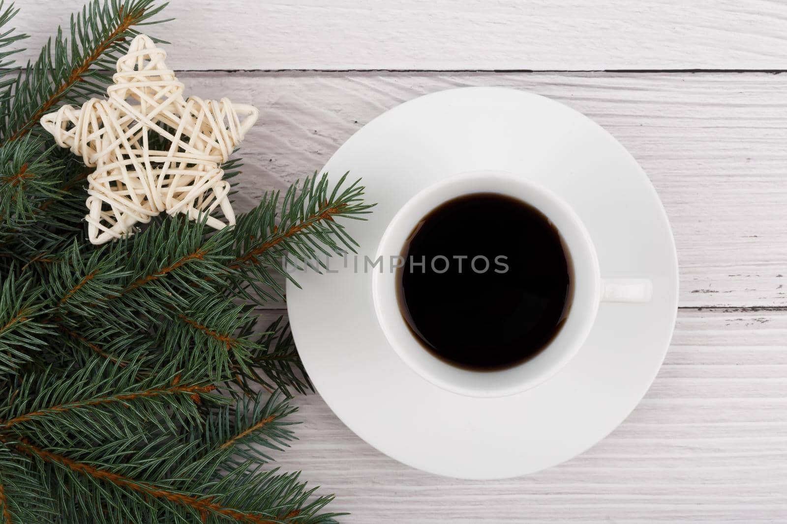 Flat lay with white ceramic coffee cup with on a plate on white rustic style wooden table decorated with Christmas tree and a star. Concept of New Year and Christmas
