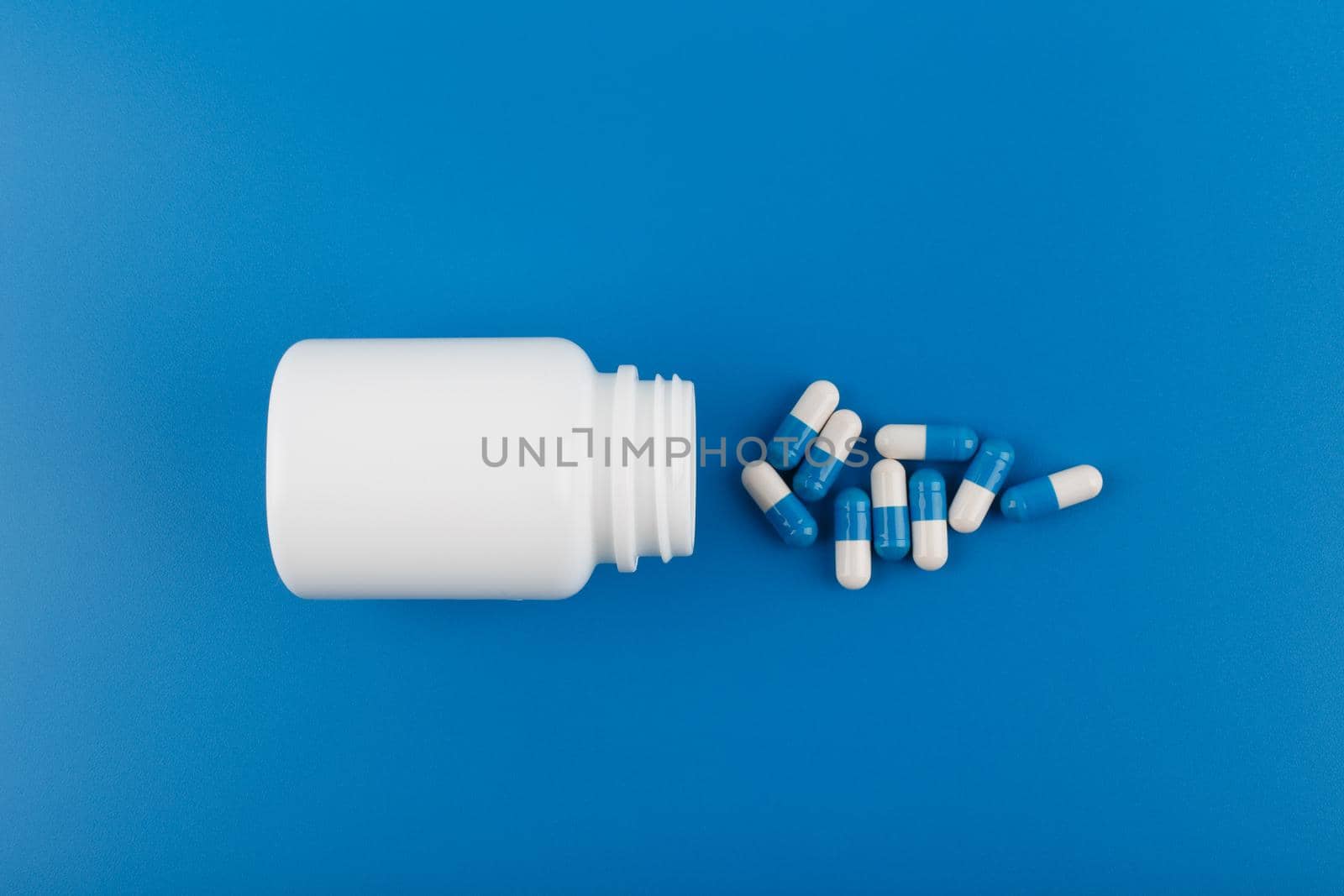 Flat lay with medication bottle and spilled pills on blue background. Concept of medication, vitamins or painkillers by Senorina_Irina