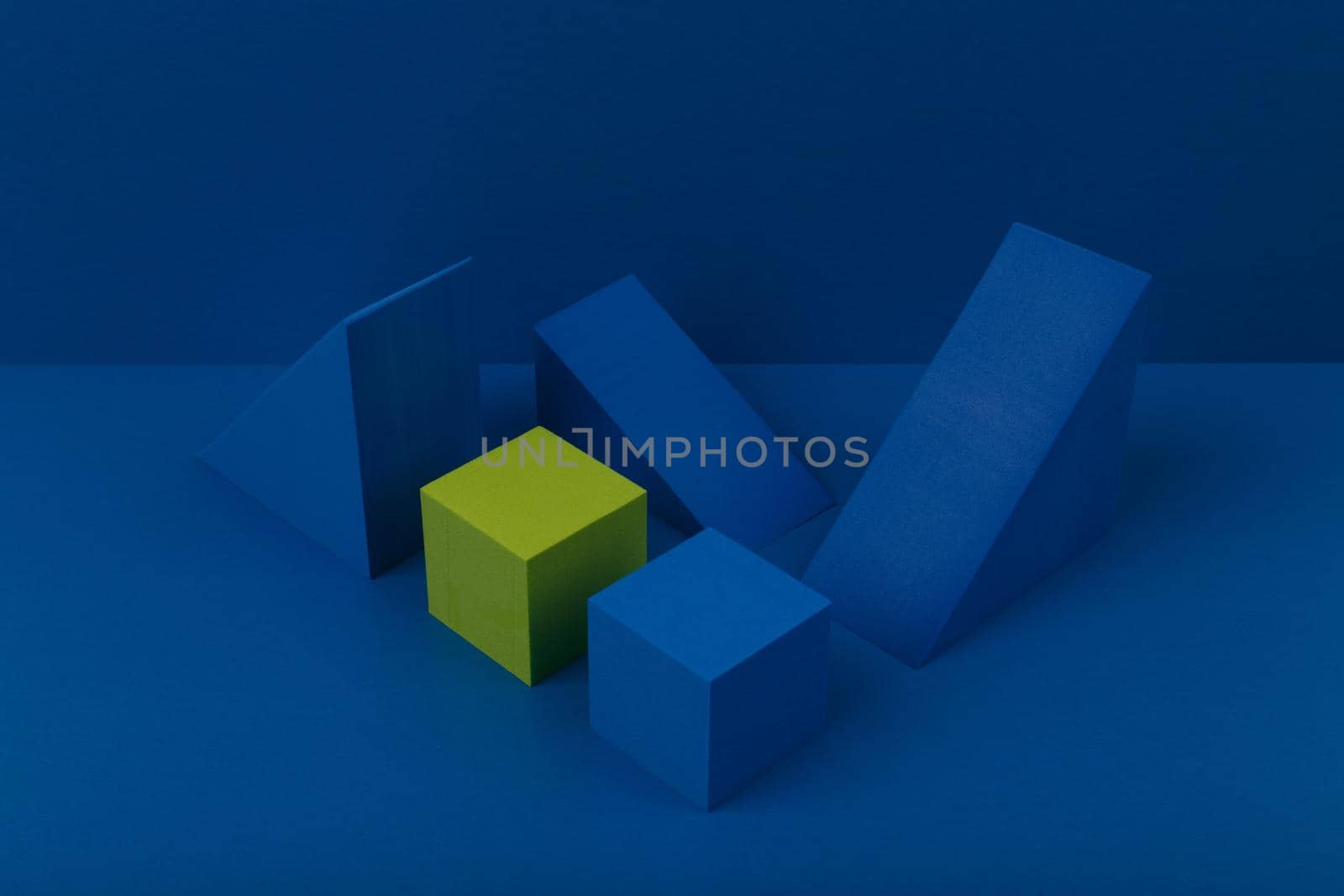 Still life with blue and green geometric figures, triangles and cubes on blue background. 