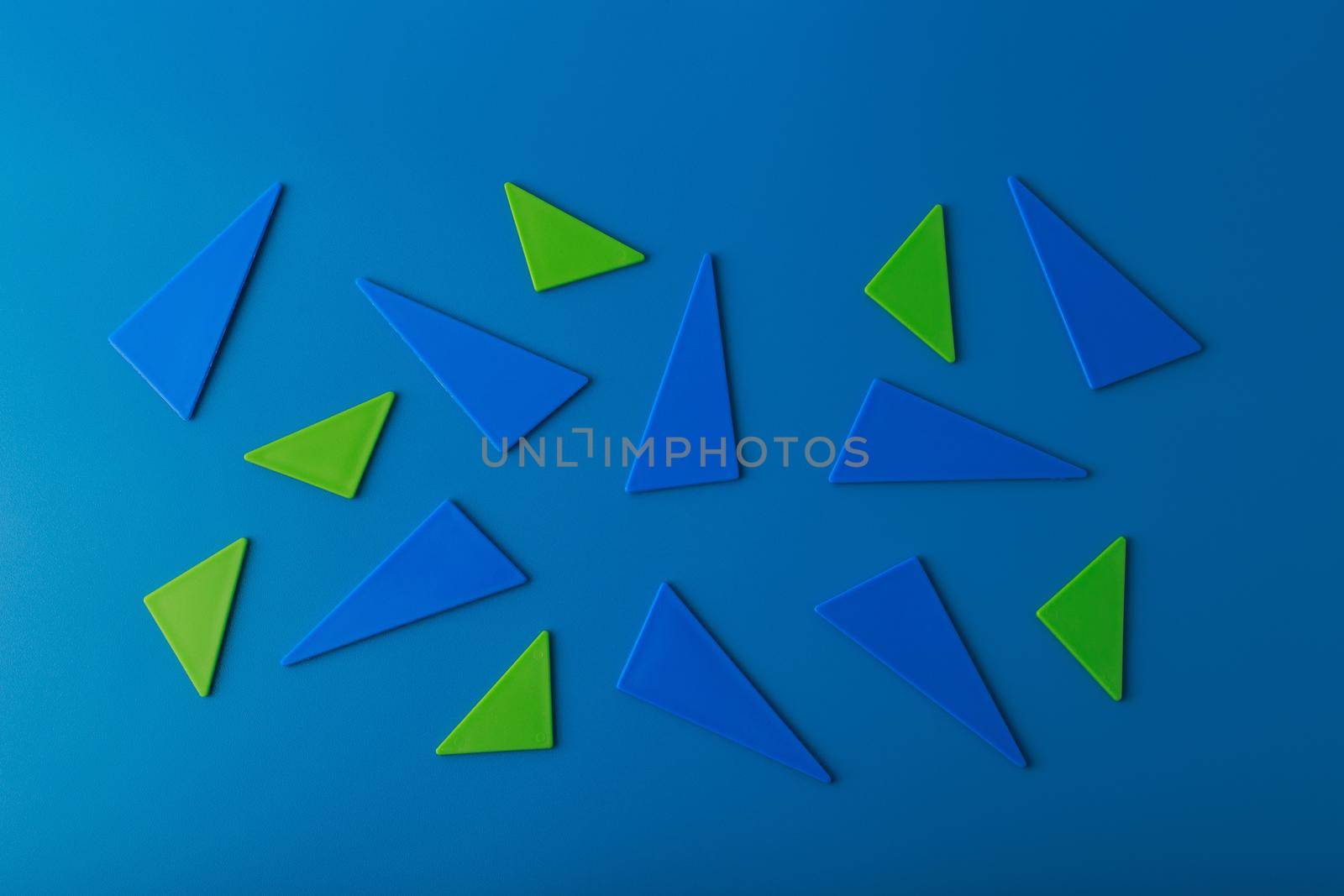 Minimalistic abstract flat lay with green and blue triangles on blue background. High quality photo