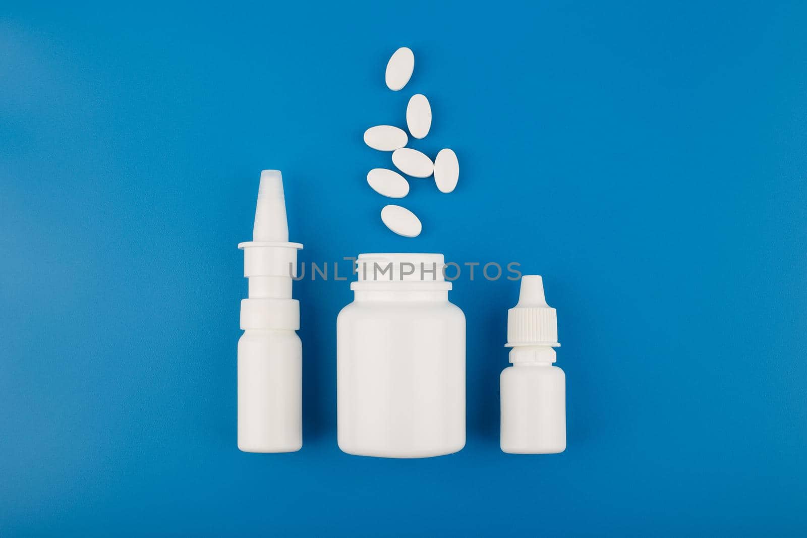 Flat lay with nose spray, medication bottle with spilled pills and eye drops in a row on blue background by Senorina_Irina