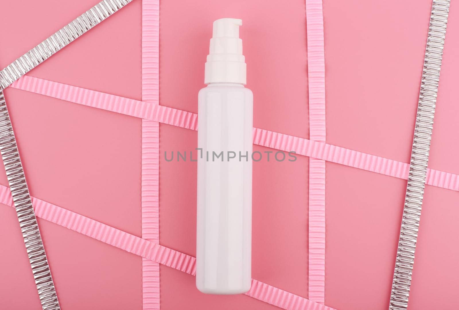 White cream tube on bright pink background with pink and silver stripes. Concept of beauty and skin care