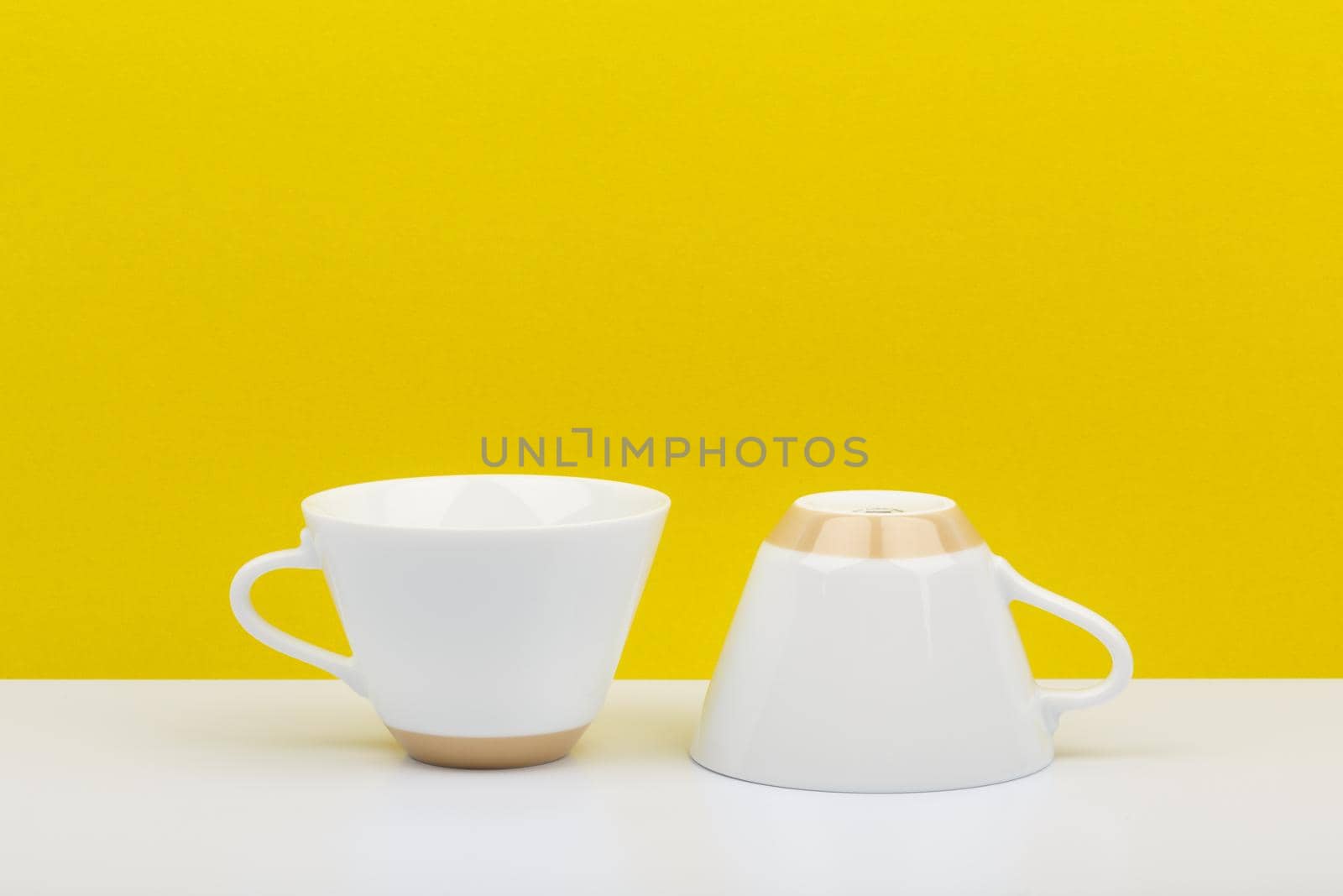 Minimalistic still life with two shiny white ceramic coffee cups on white table against bright yellow background with space for text. High quality photo