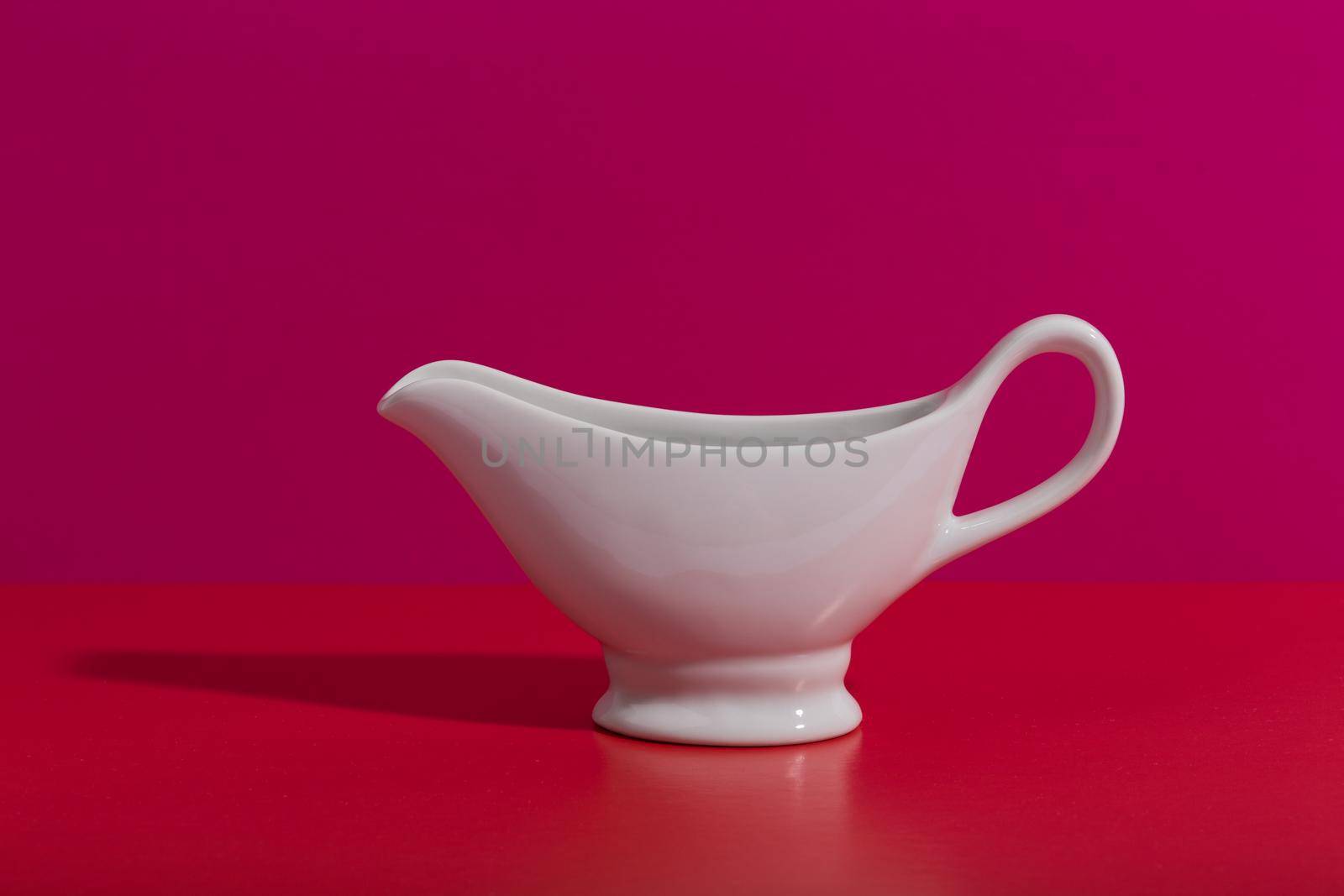White ceramic sauce boat on creative red and pink background with space for text by Senorina_Irina