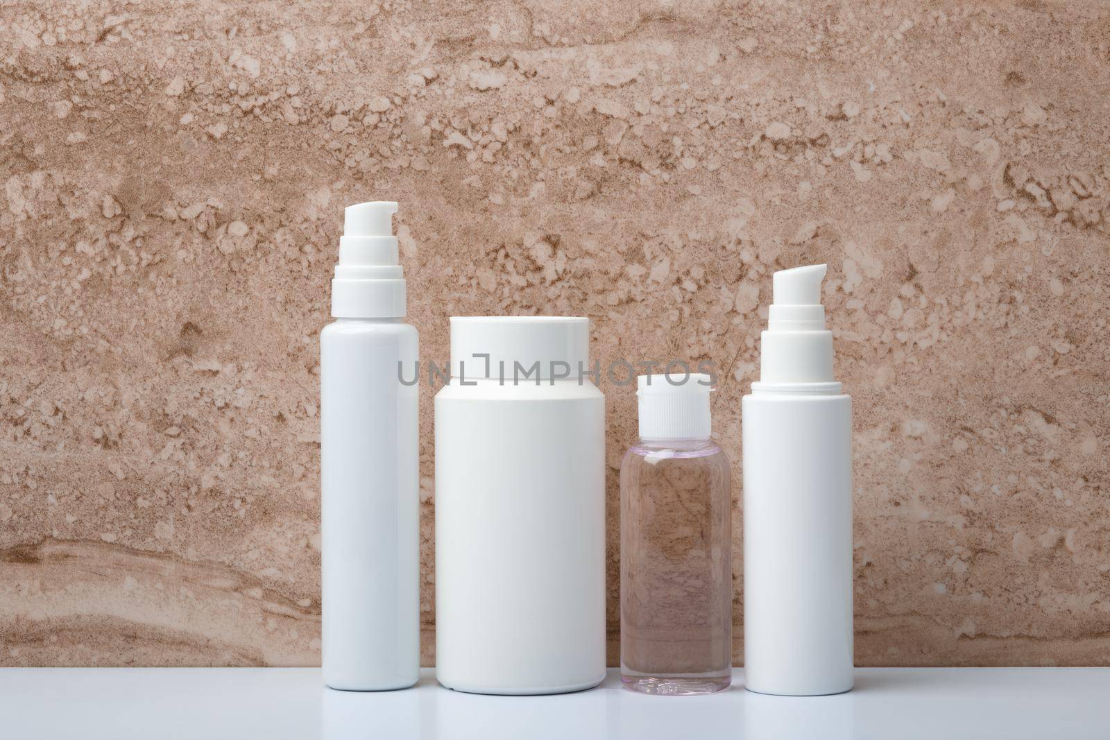 Minimalistic still life with unbranded beauty products in white glossy tubes on white glossy table against marble background. High quality photo