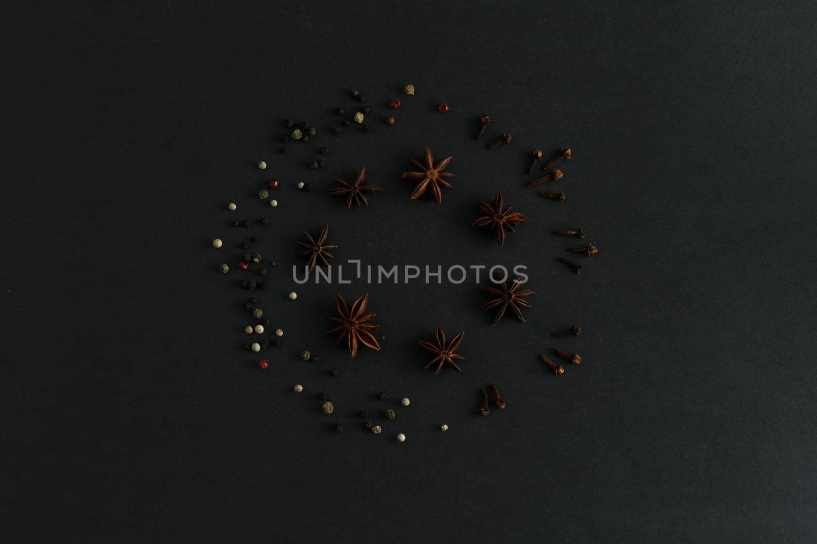 Round composition of anise stars, colorful pepper and clove sticks on black background