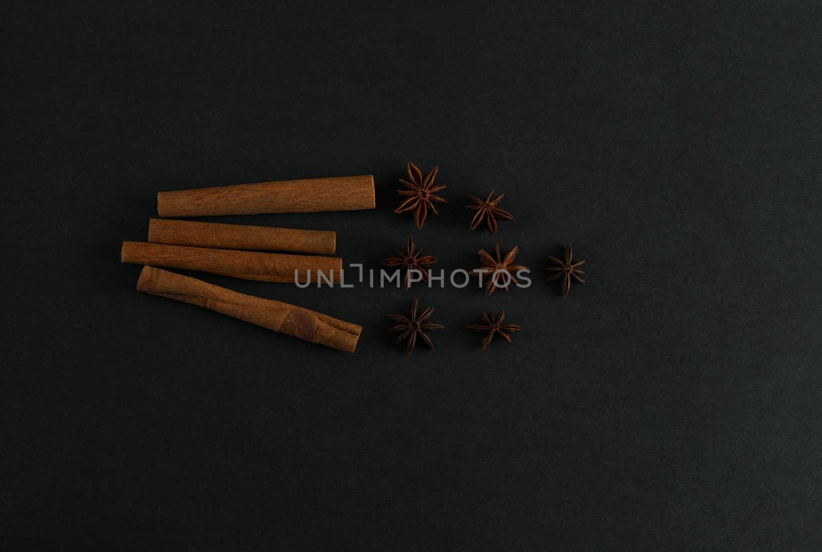 Four big cinnamon sticks and anise stars flatlay on black background