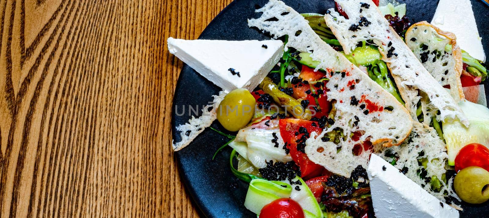 Salad on a plate. Salad with cheese, bread, ofochas and fruits on a black plate.