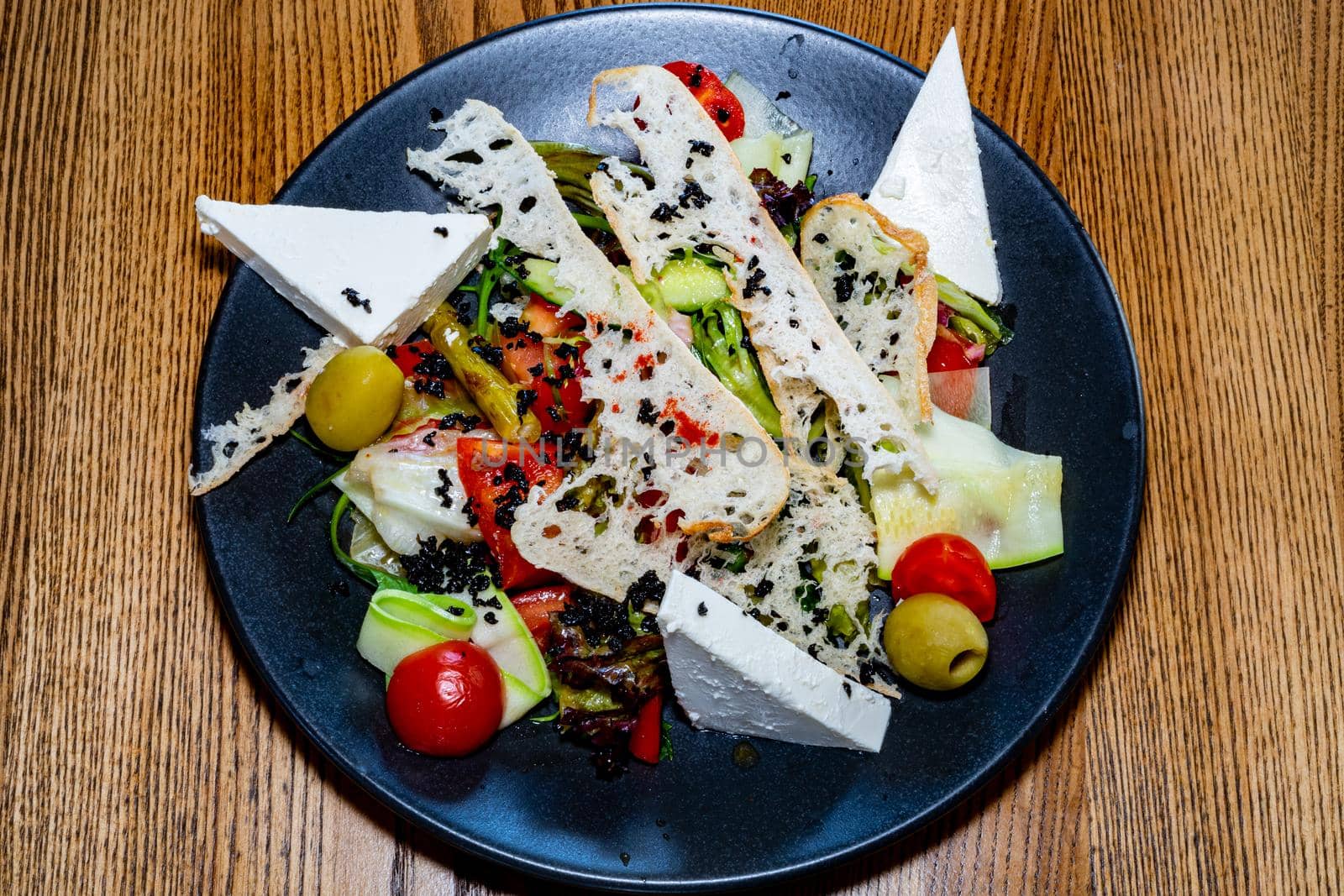 Salad on a plate. Salad with cheese, bread, ofochas and fruits on a black plate.