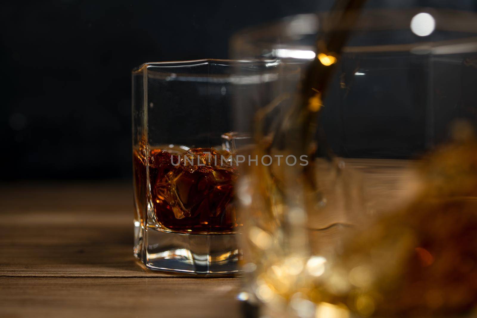 Whiskey drinks on wood with ice cubes and splash.