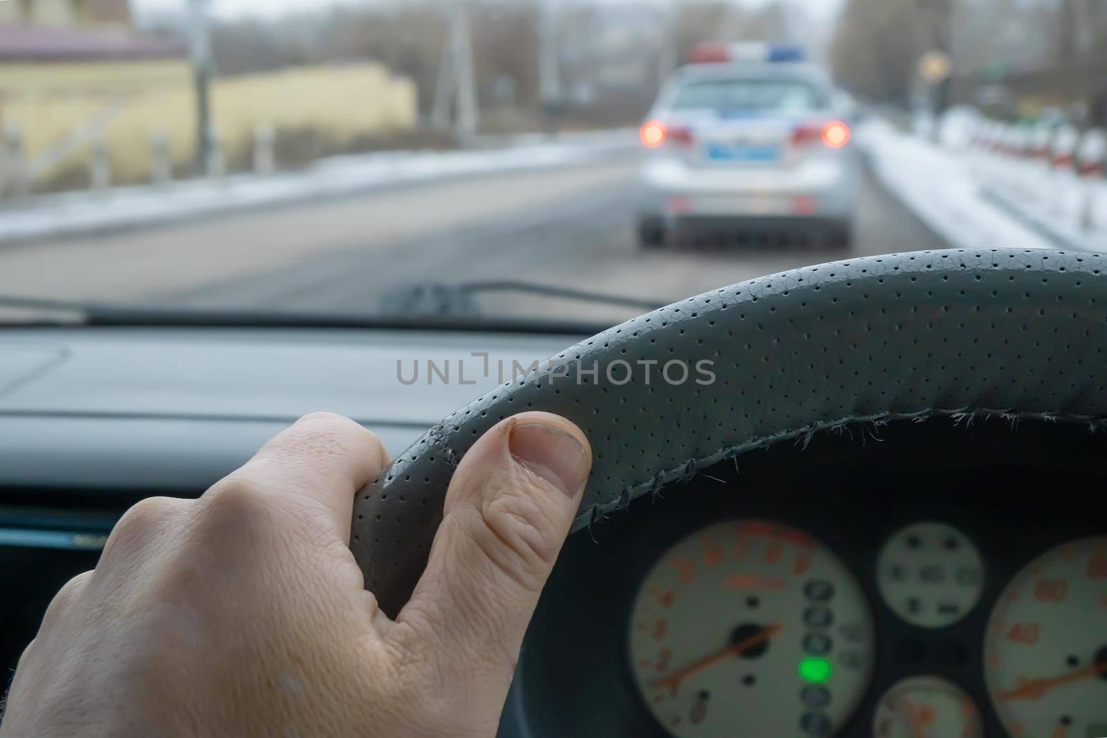 the driver's hand on the steering wheel of a car that is driving on the road behind a police car