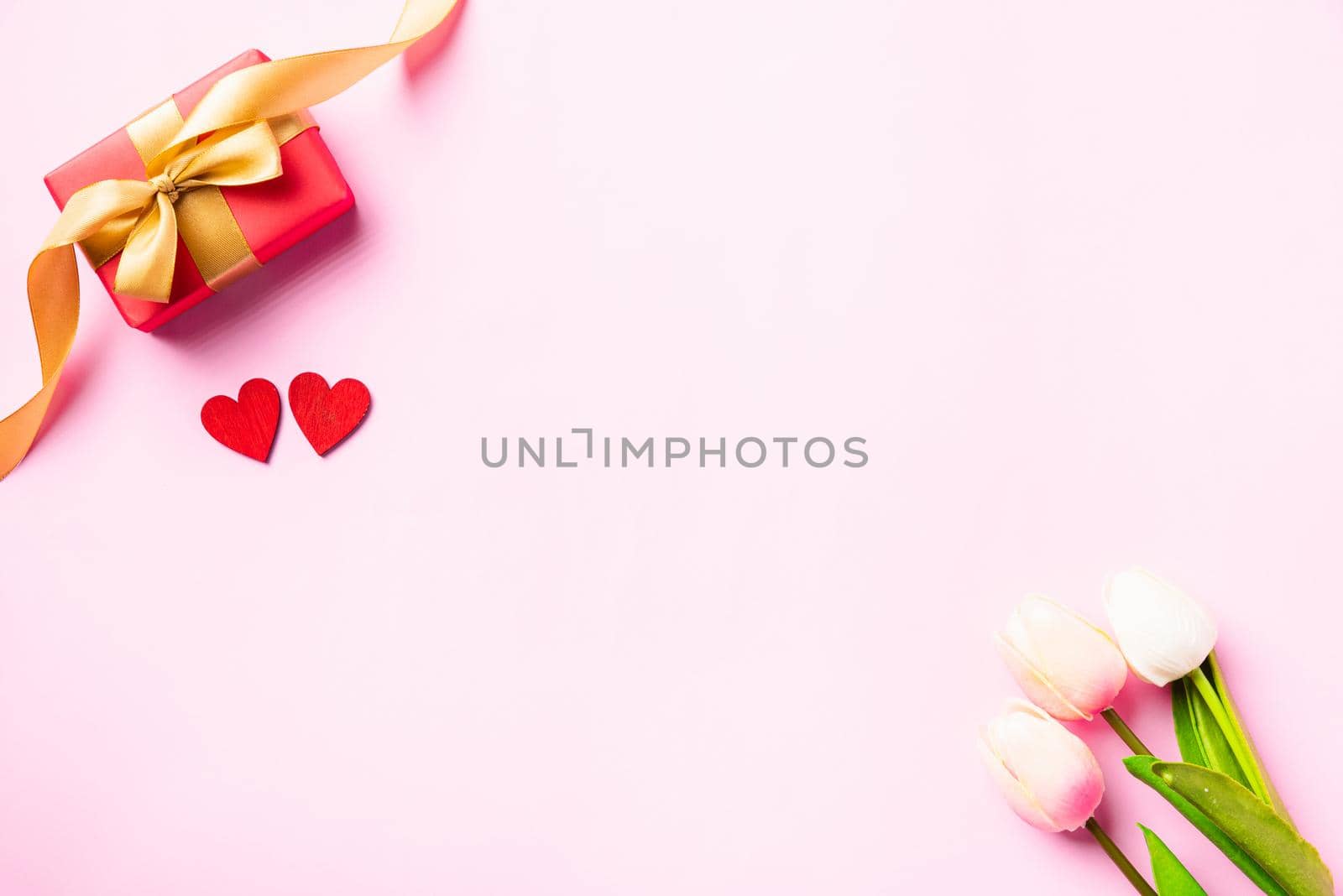 Happy Valentine's day composition background concept. Red gift box with a golden bow ribbon and wood red hearts for love isolated on pink background with copy space. Top View from above