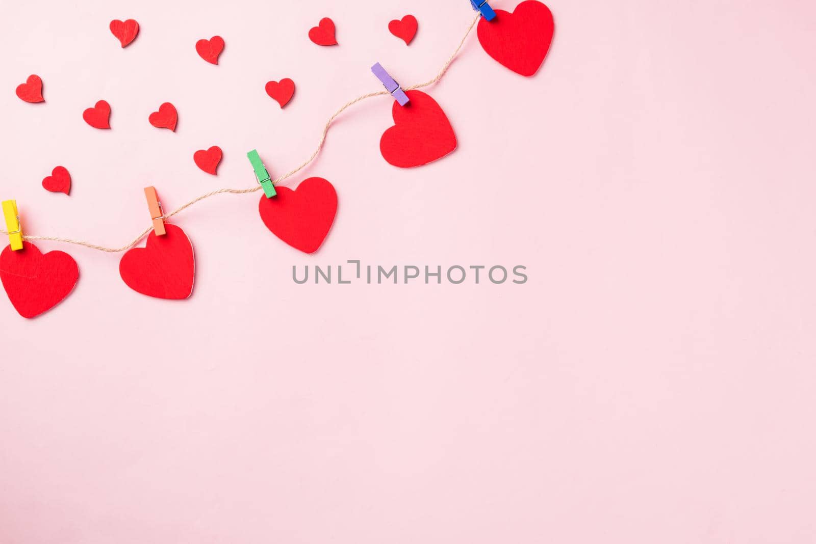 Happy Valentine's day background. red heart shaped valentines decoration hanging with paper clips on the rope for love composition greeting card isolated on pink background with copy space