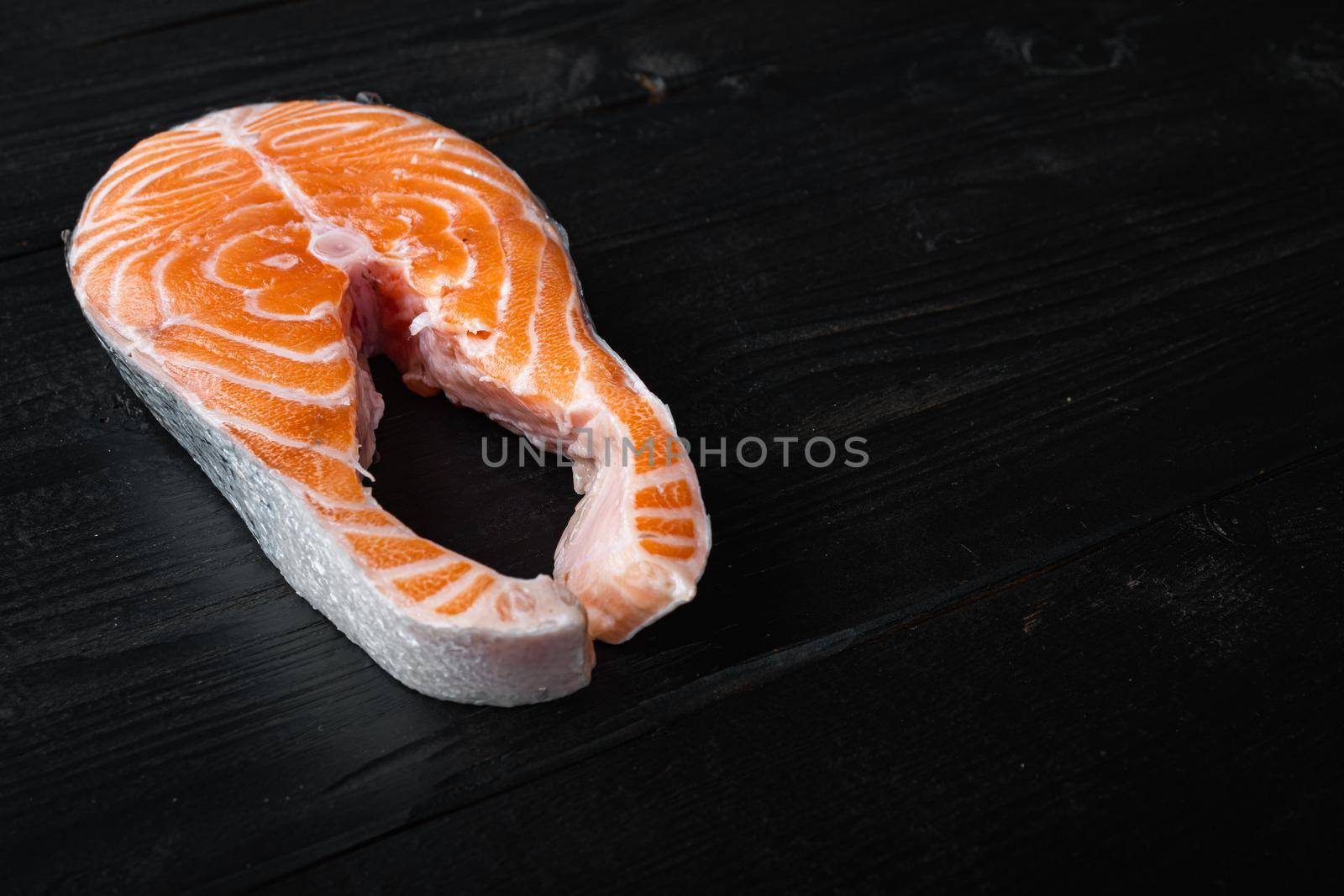 Raw trout steak, on black wooden surface with space for text.