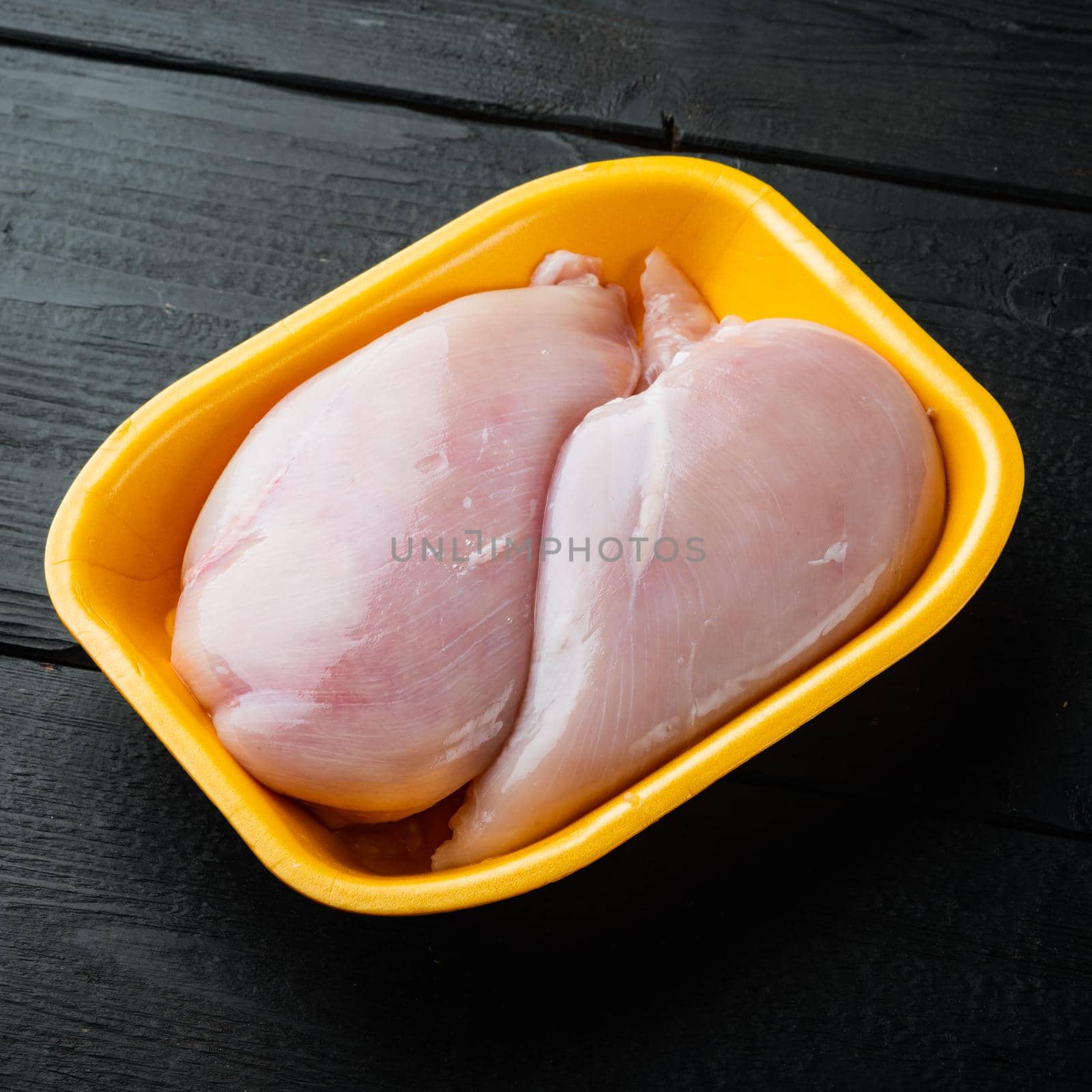 Fresh chicken breast meat in open tray, on black wooden table